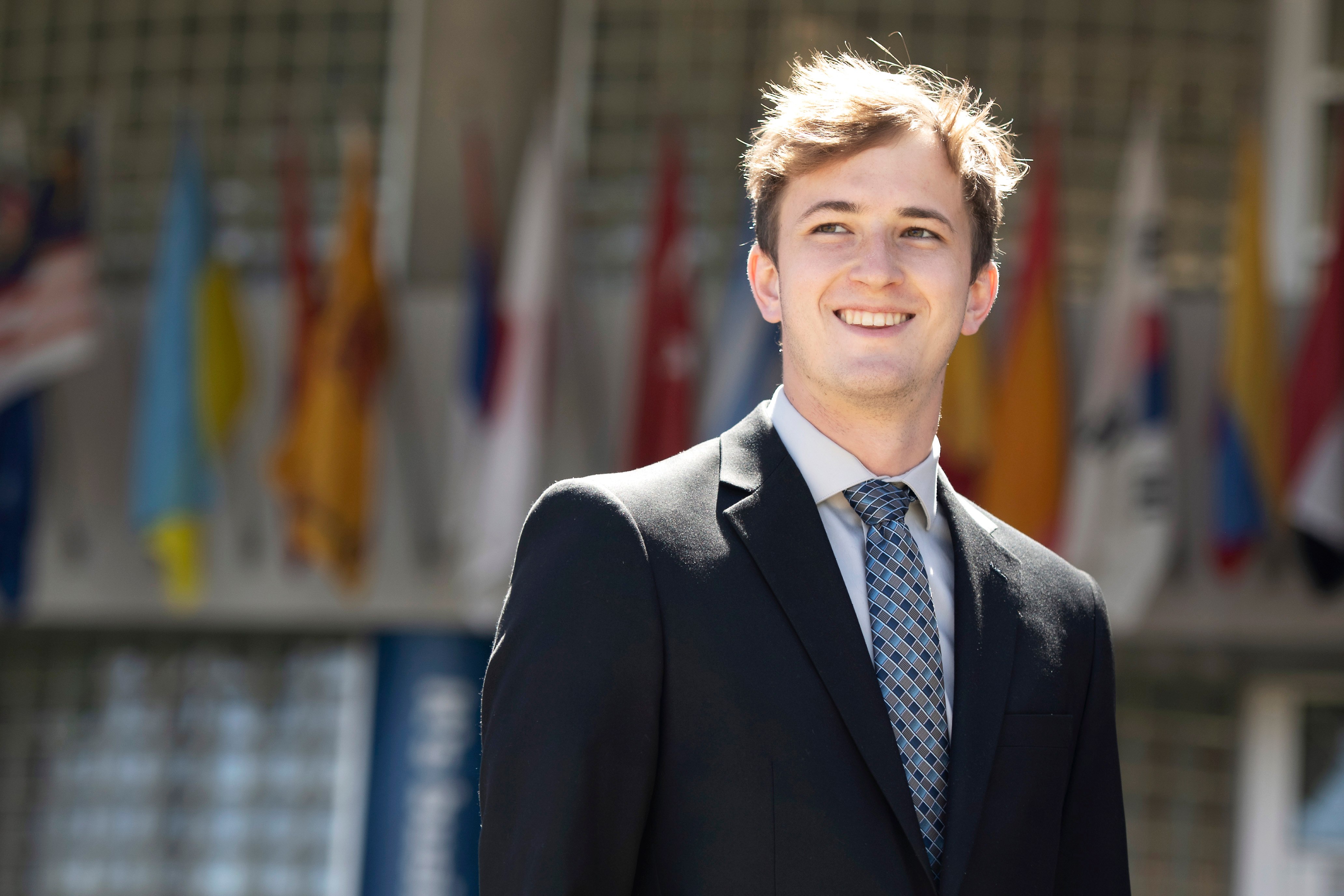 A Drake student in a suit stands in front of a building with international flags on the exterior