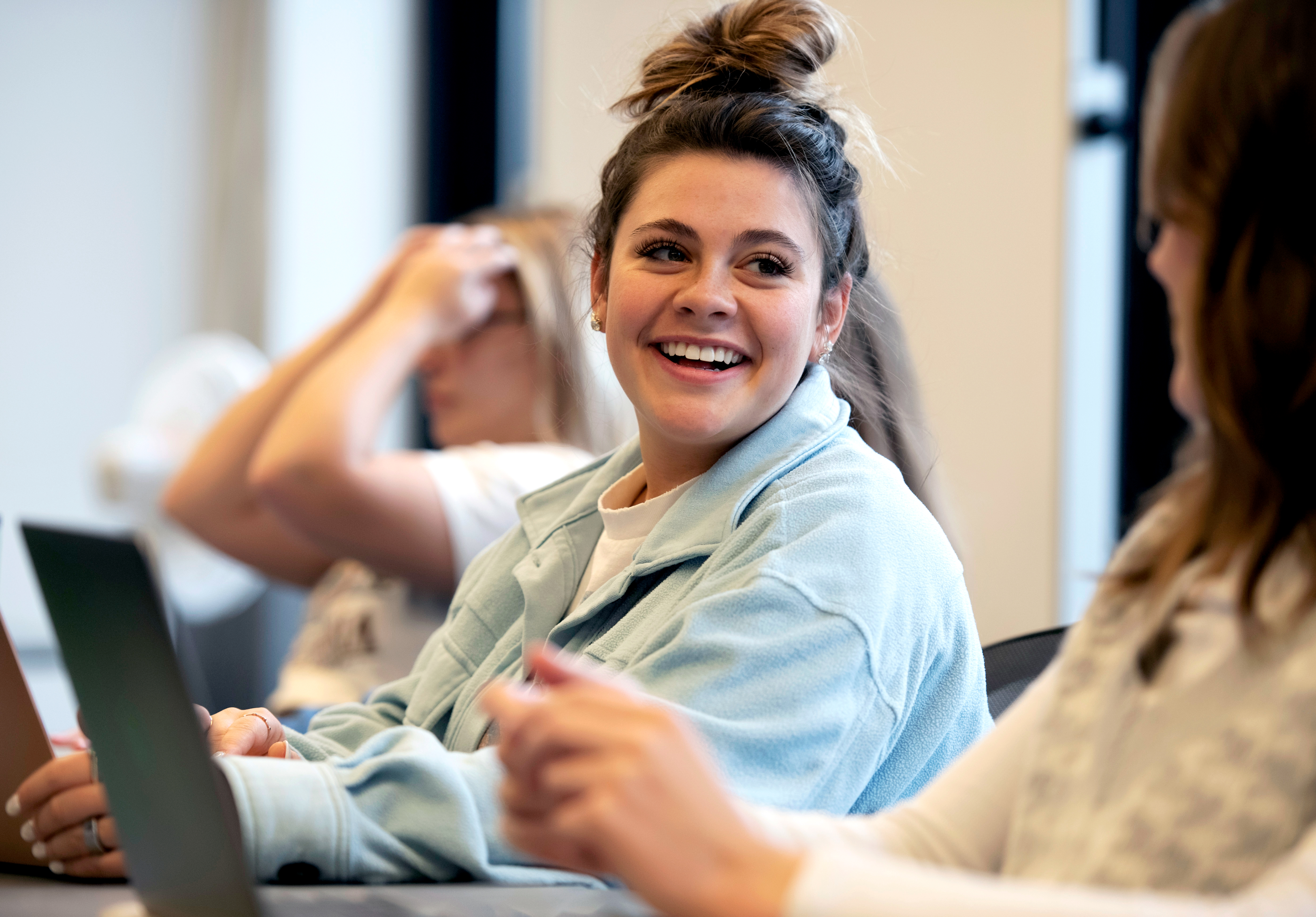Drake students smile at each other while taking notes on their laptops in class