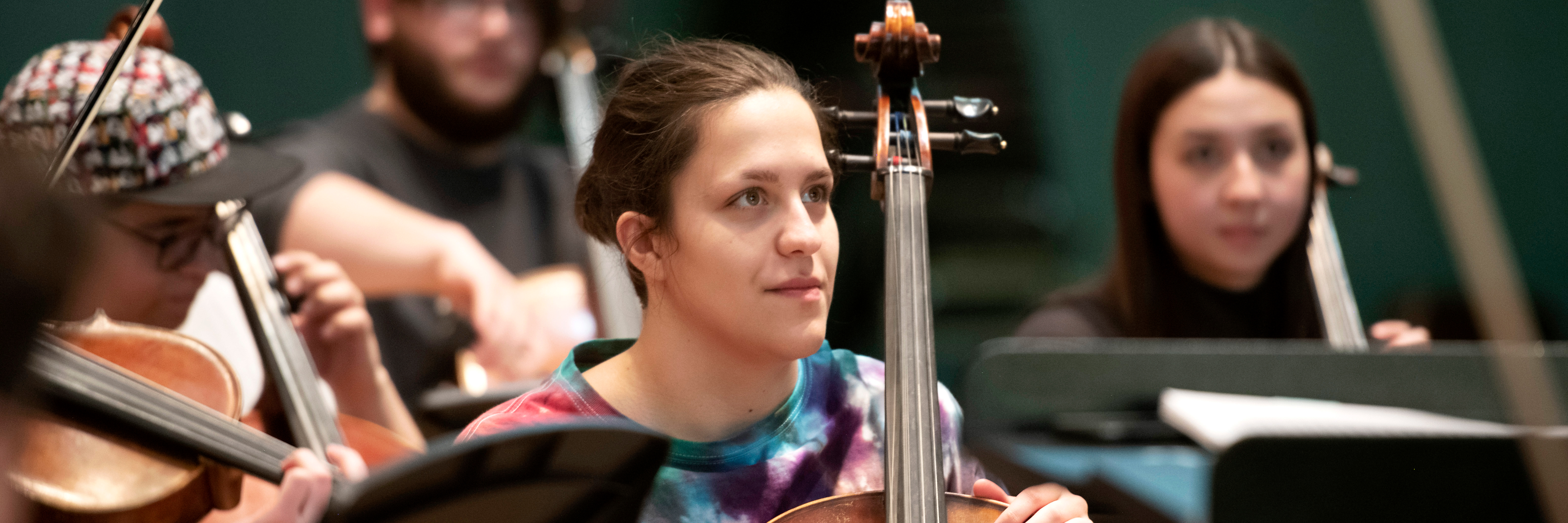 A cello student watches a conductor in one of Drake's musical ensembles
