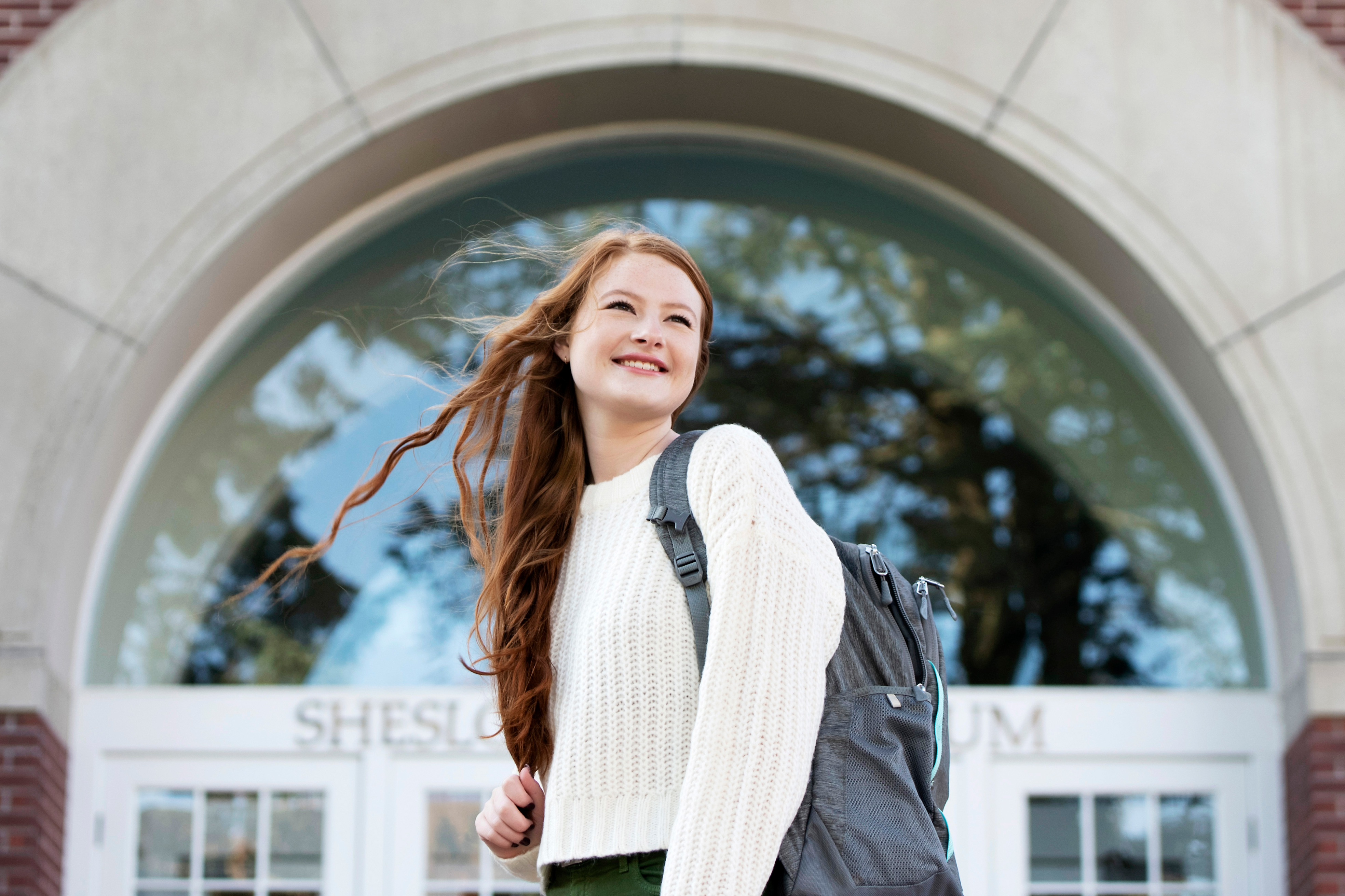 A student with a backpack looks left while standing in front of Drake's Sheslow Auditorium