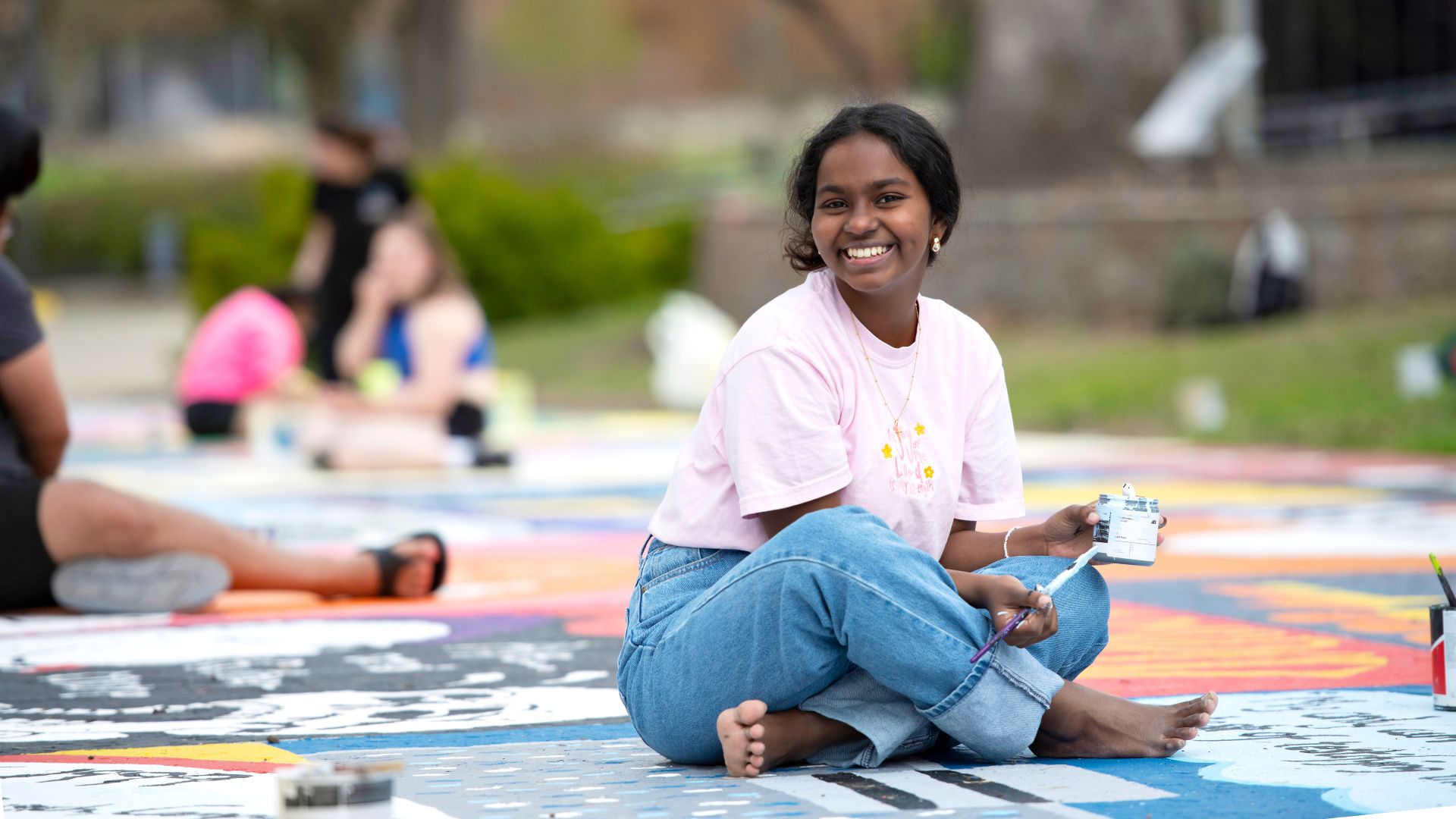 A Drake student smiles while sitting on the ground for a group painting project