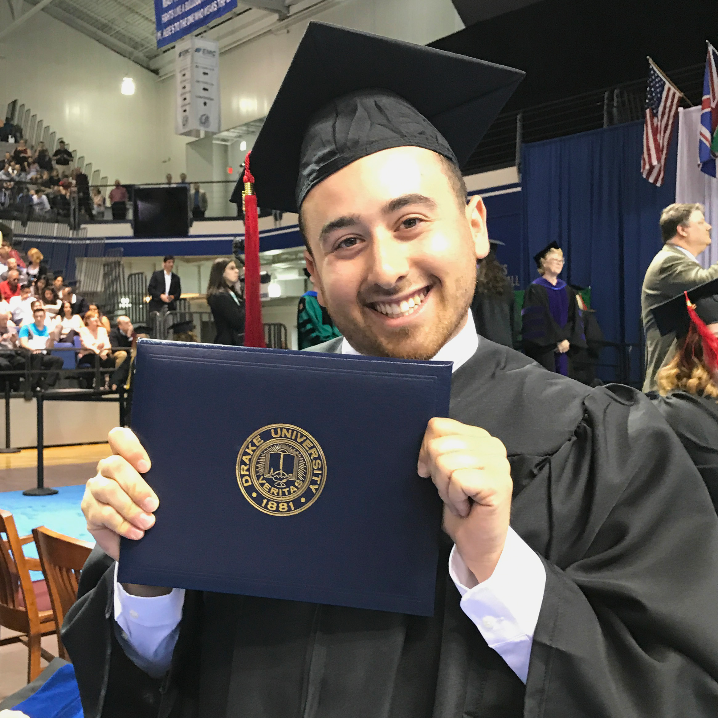 A student in a black cap and gown presents their diploma from Drake University