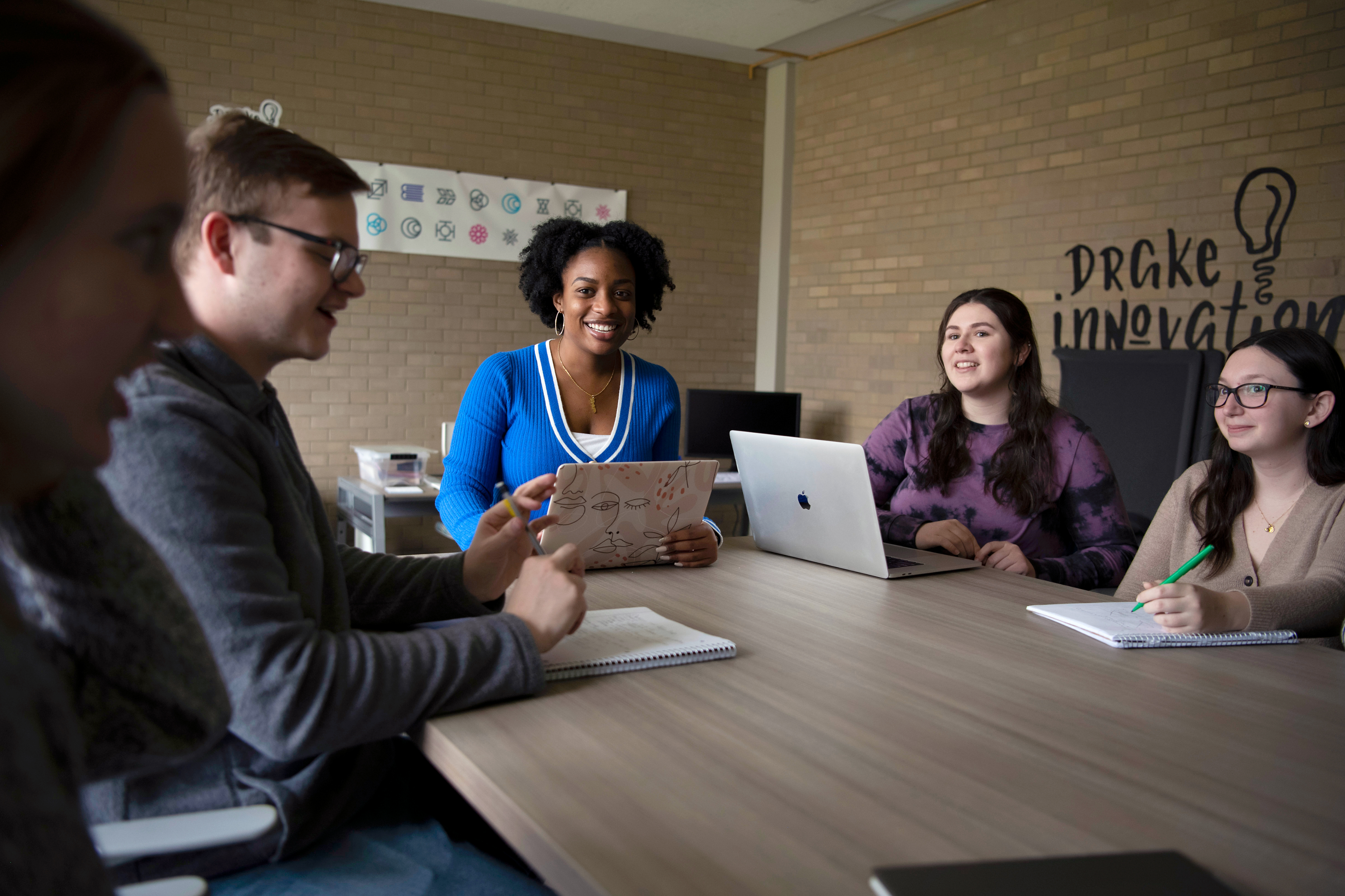 A group of students sit around a table with their laptops for a class in Drake's innovation space