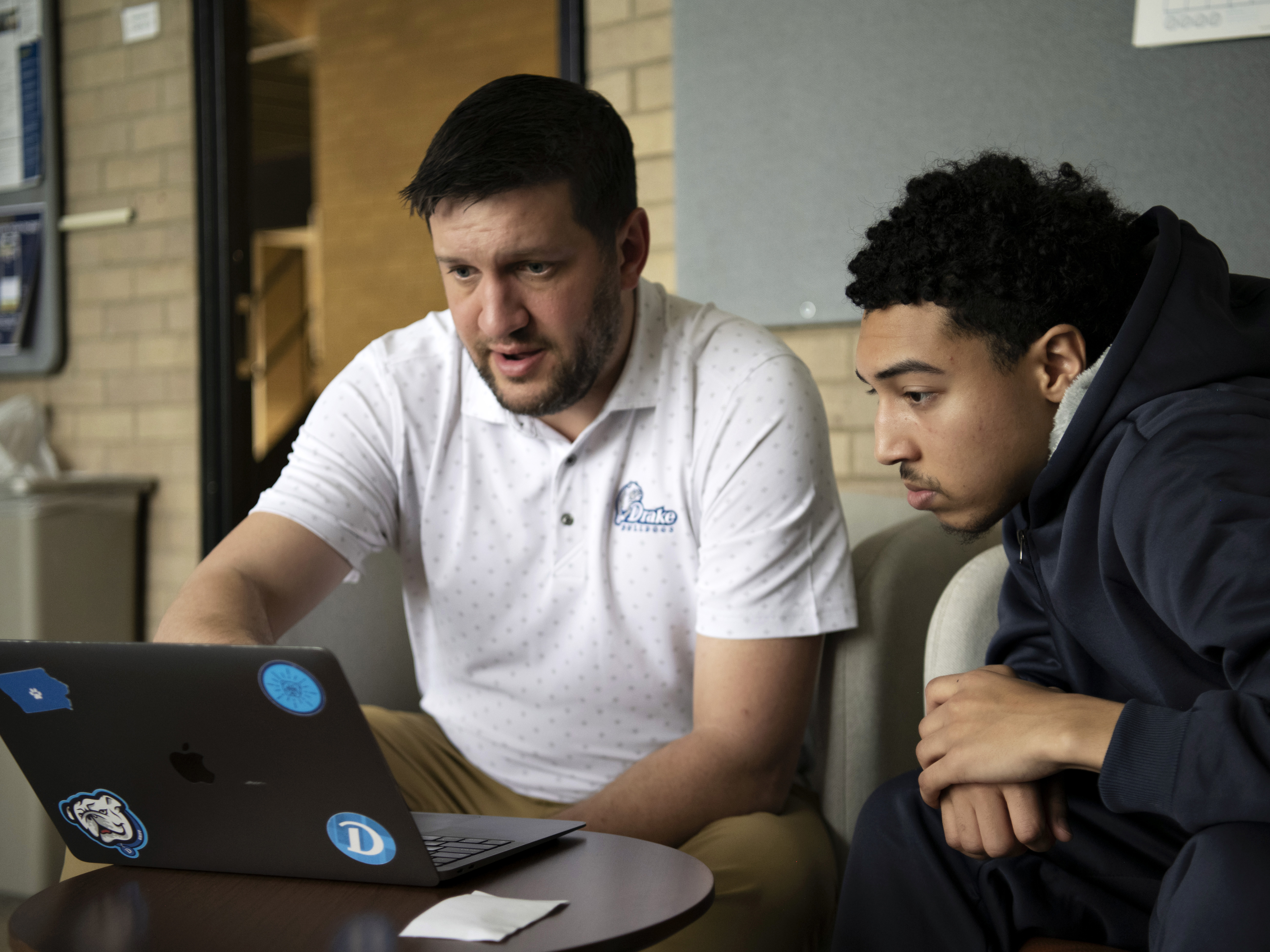 Pointing to a laptop on a short table, a faculty member explains a concept to a Drake student