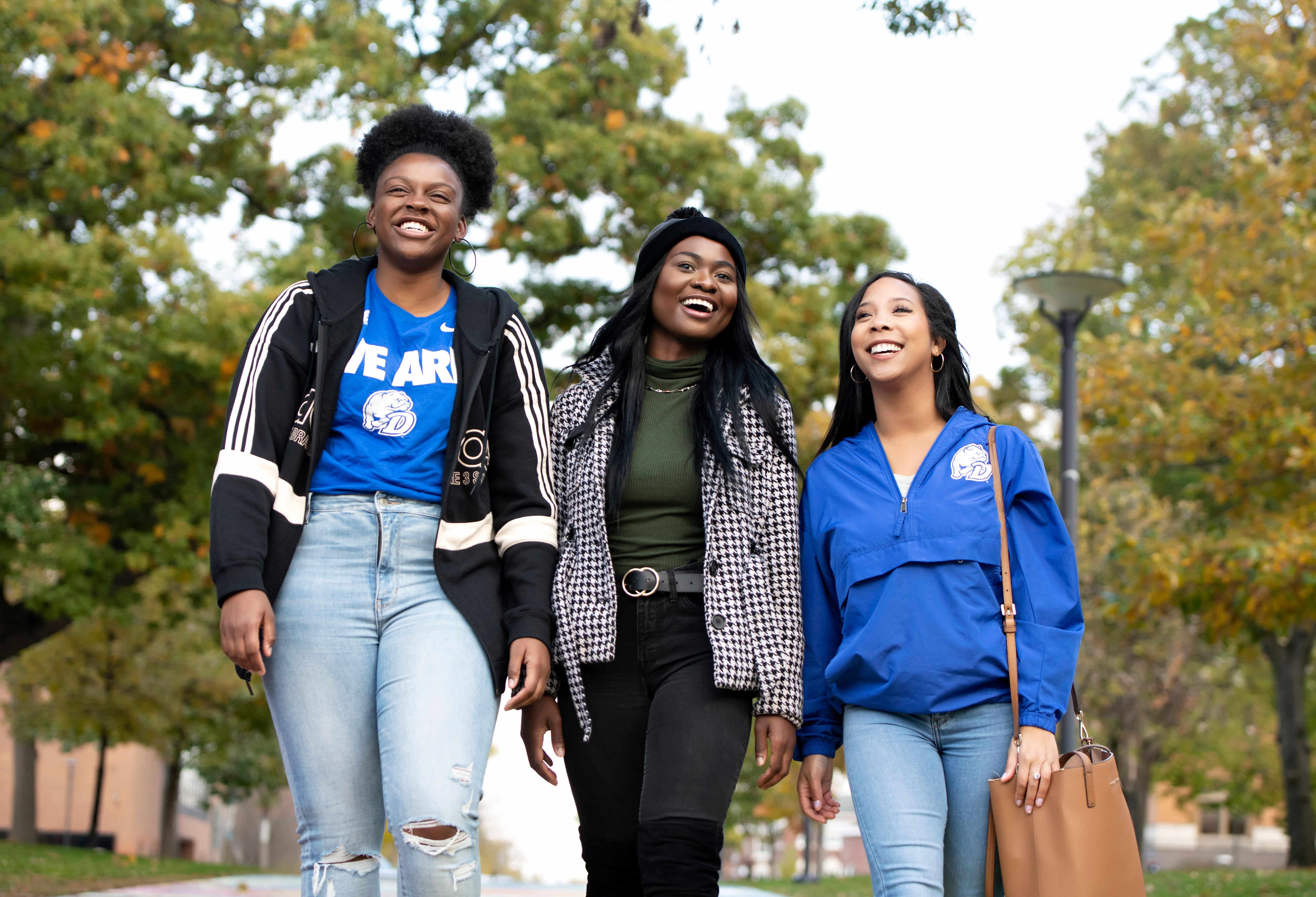 Three Drake students walk and smile along a path, with nearby trees displaying the early signs of fall
