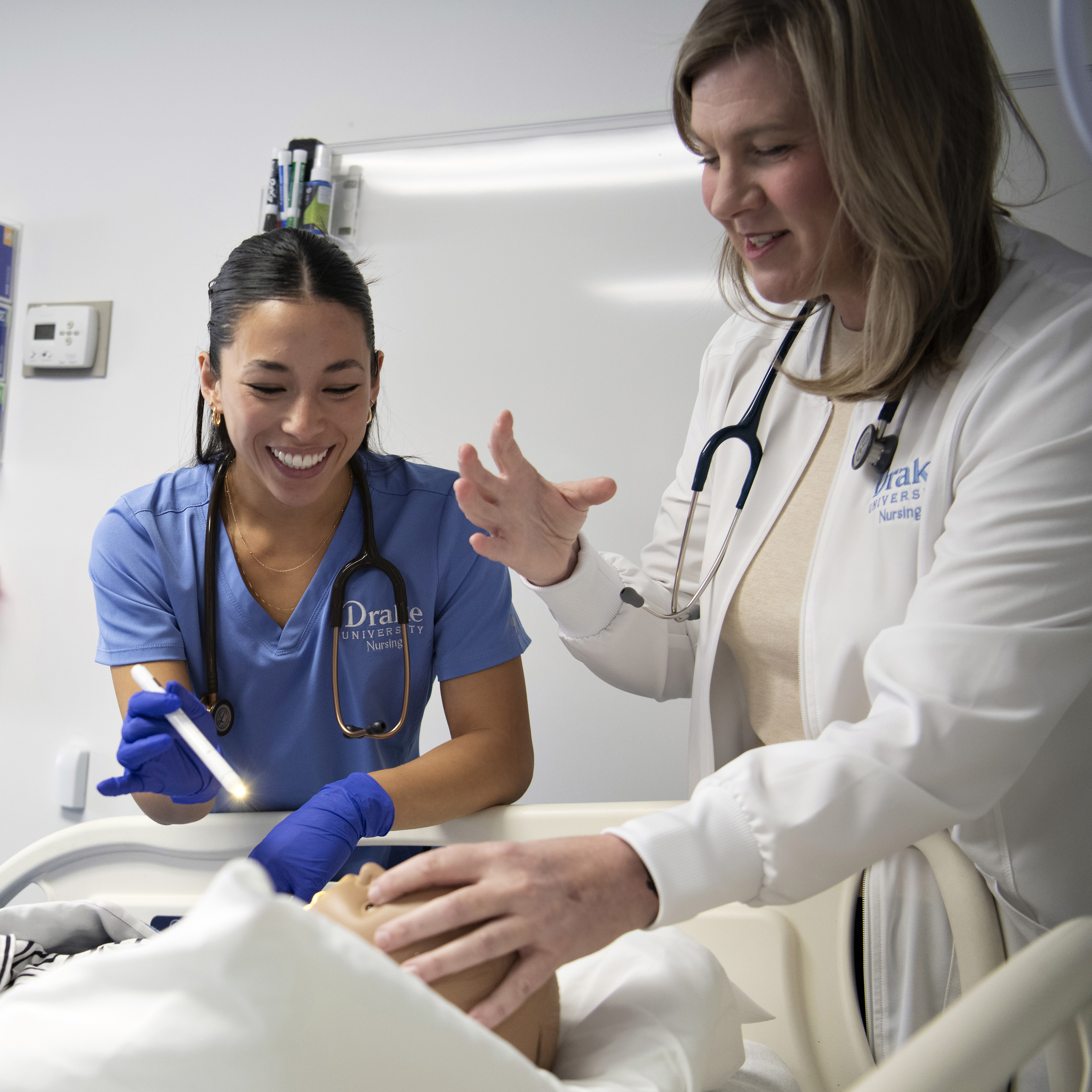 A teacher and a student, both with stethoscopes, practice assessing a patient in one of Drake's simulation labs