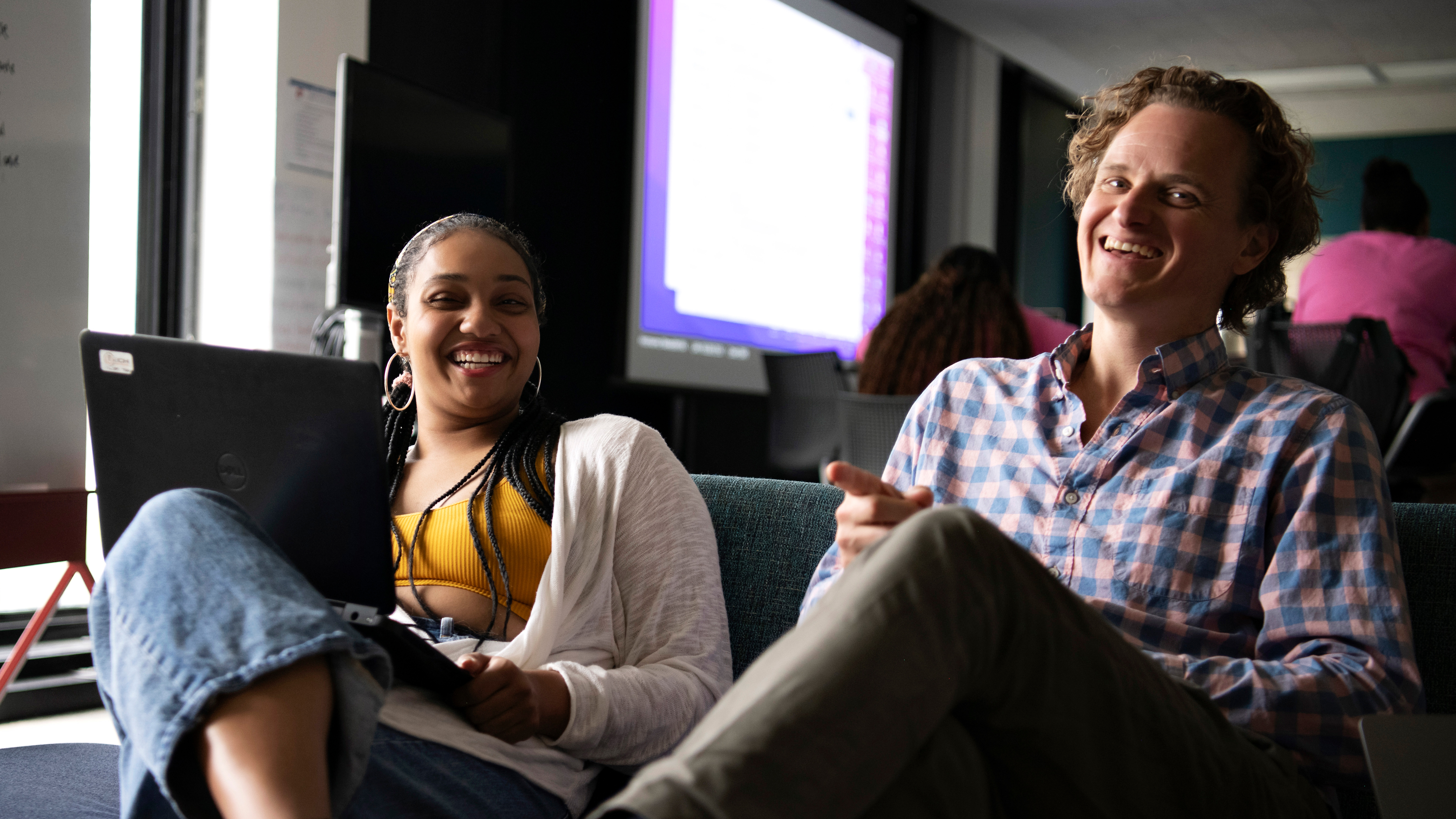 In a common area, a faculty mentor meets with a Drake student, who is holding a laptop