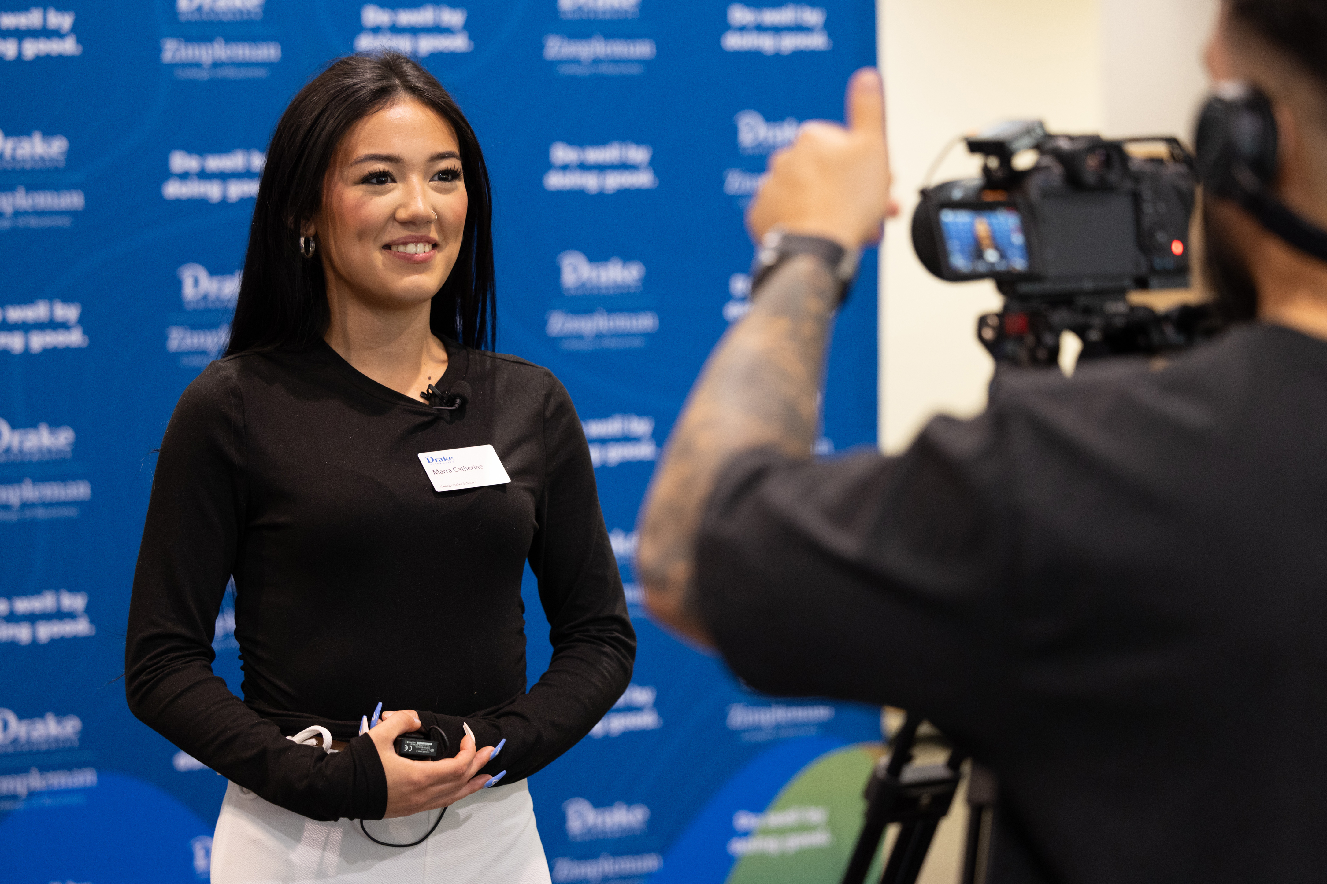 A student attending Drake's Biz for Good seminar stands in front of a wall printed with the school's logo