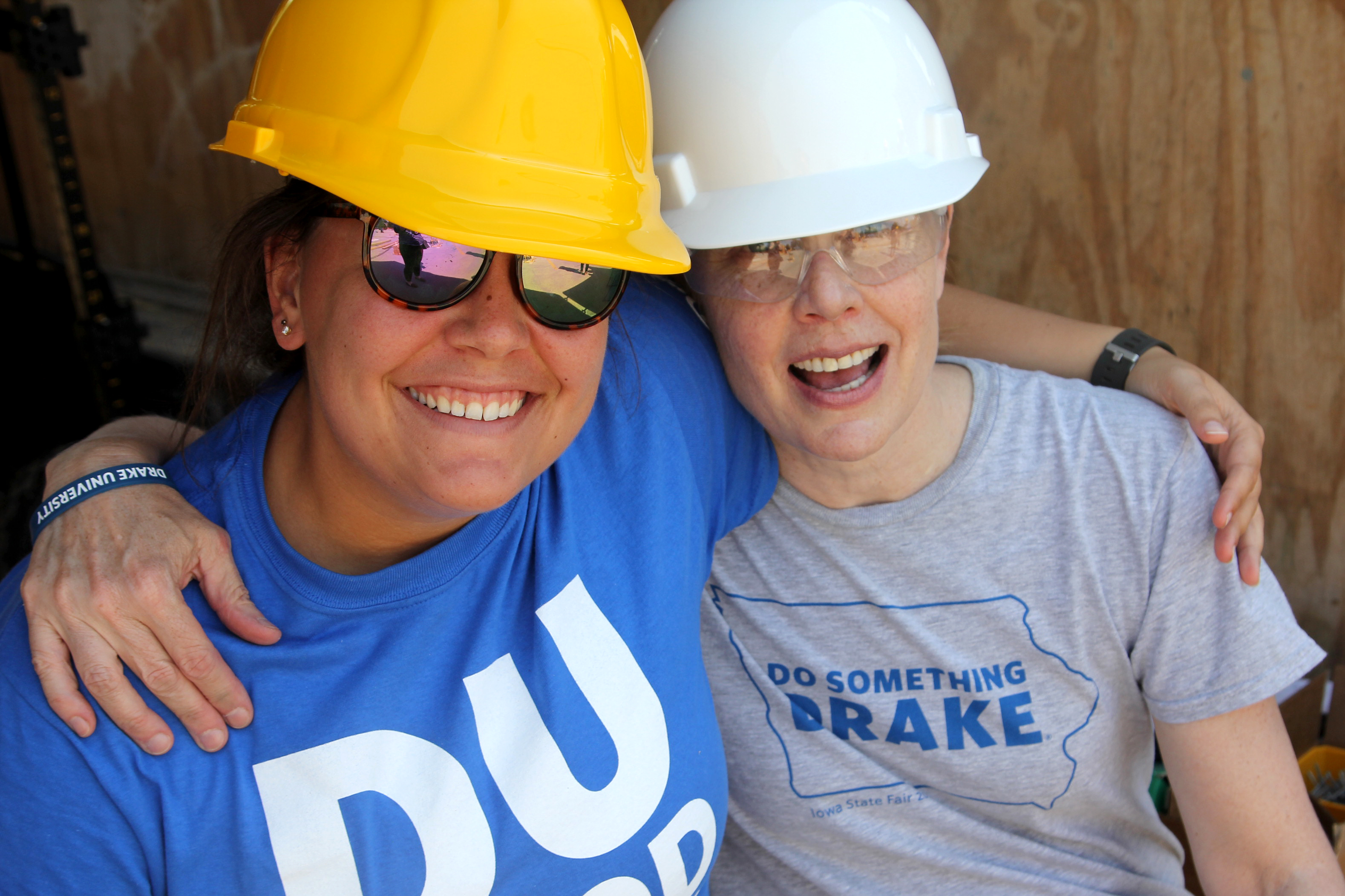 Two Drake students, in glasses and hard hats, sit arm in arm during DU Good Day