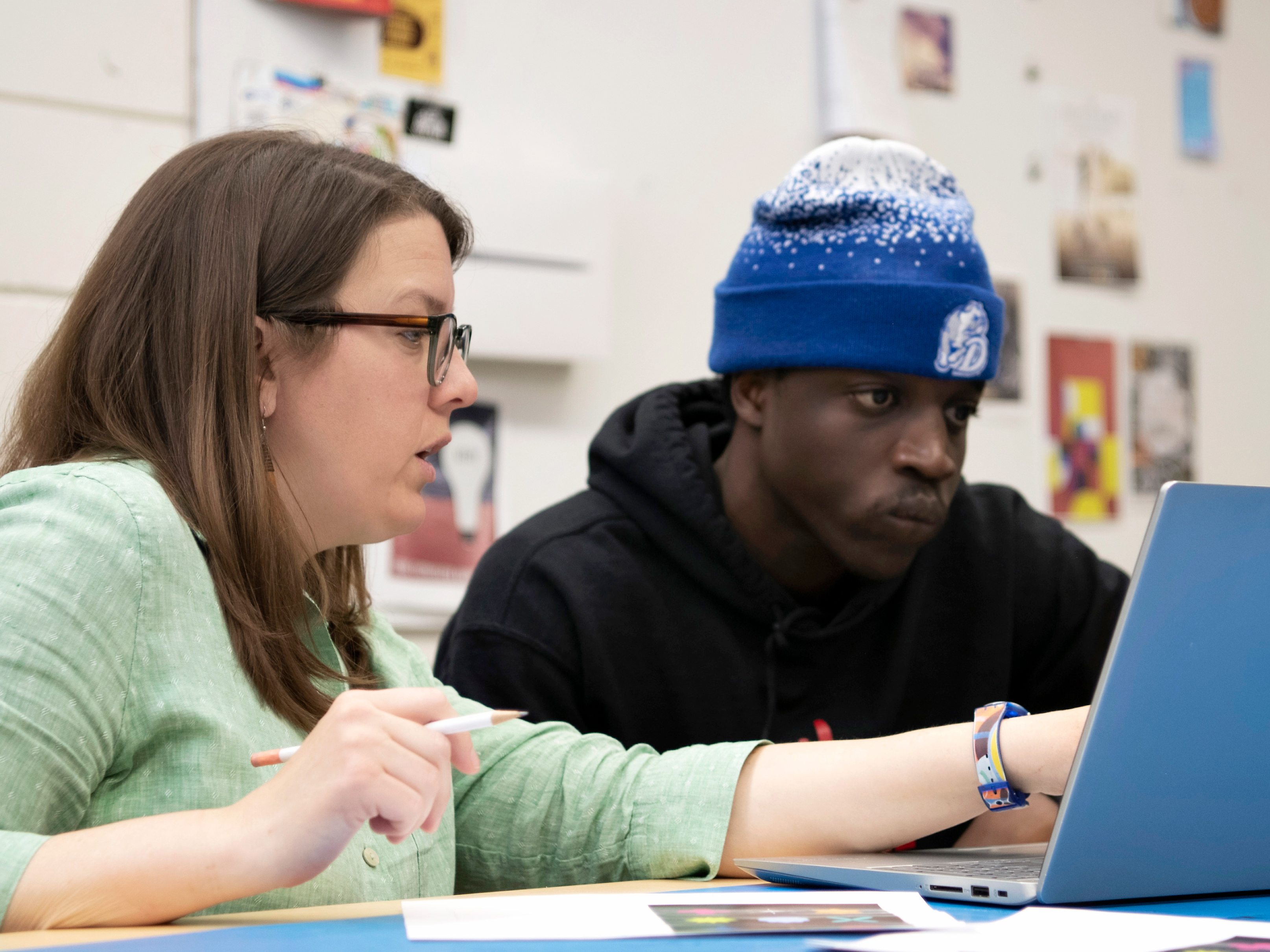 A professor points to a Drake student's laptop screen, explaining a concept during a one-on-one tutoring session