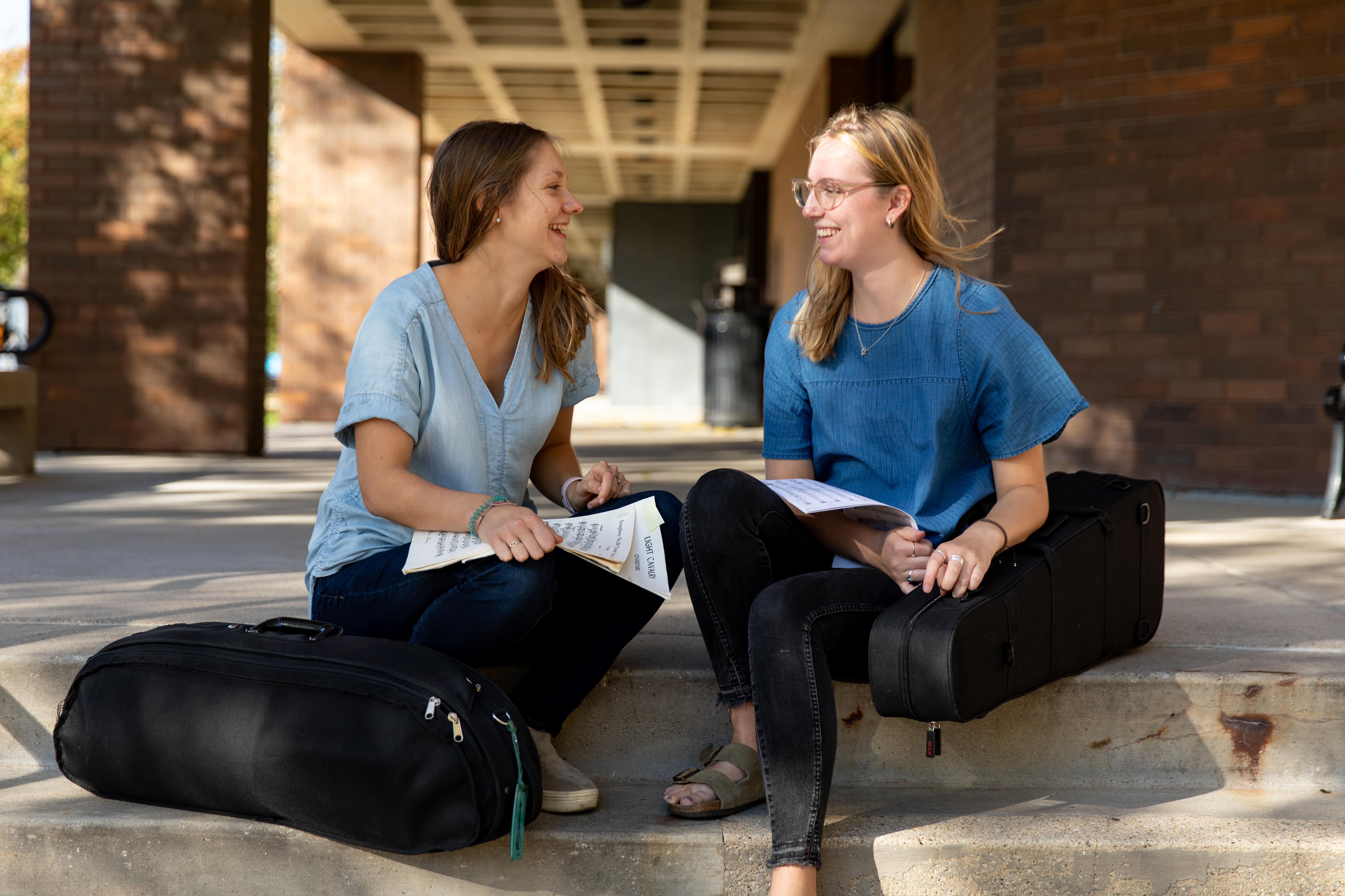 Two Drake Music students with violin cases sit on a step to converse over a piece of music