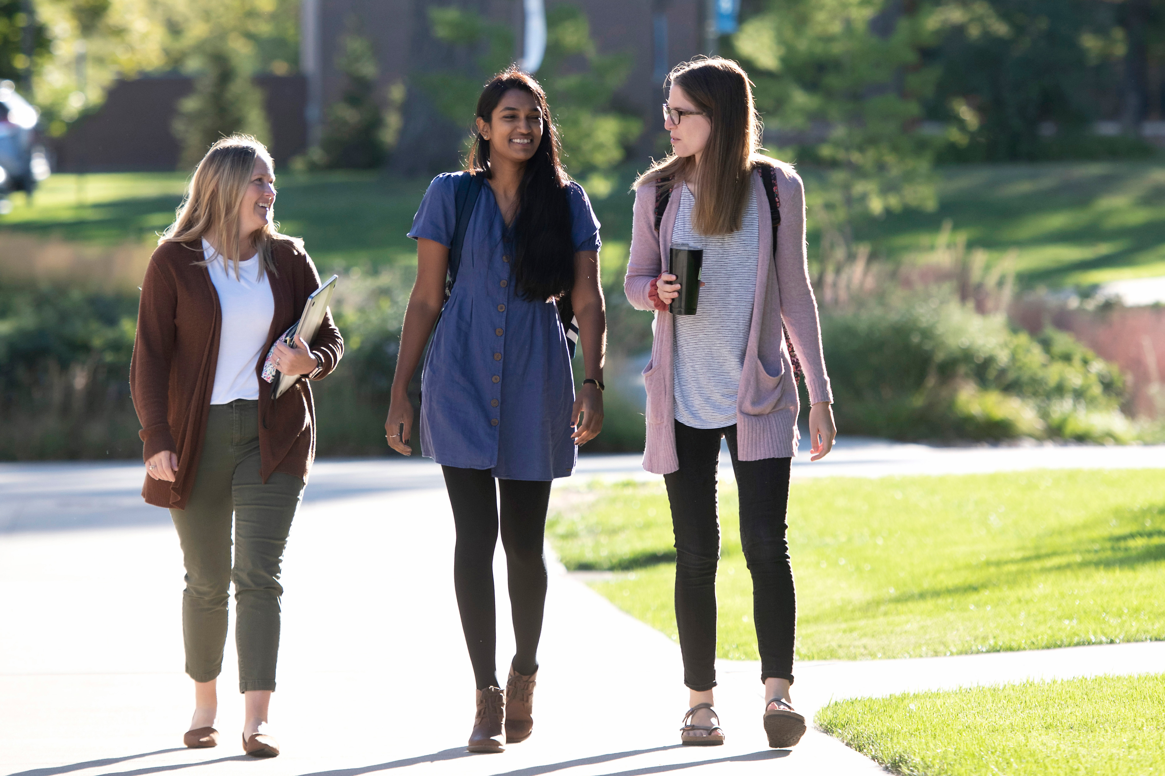 Working adult students, holding backpacks or mugs, converse during a walk through campus