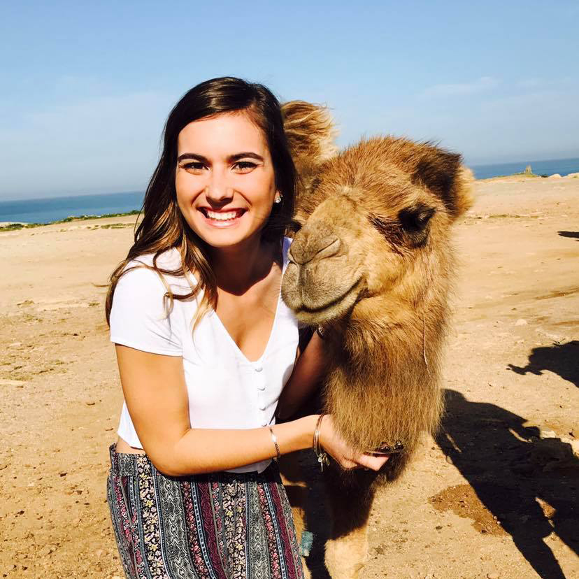 A Drake student on a study abroad trip poses with a camel in a desert environment