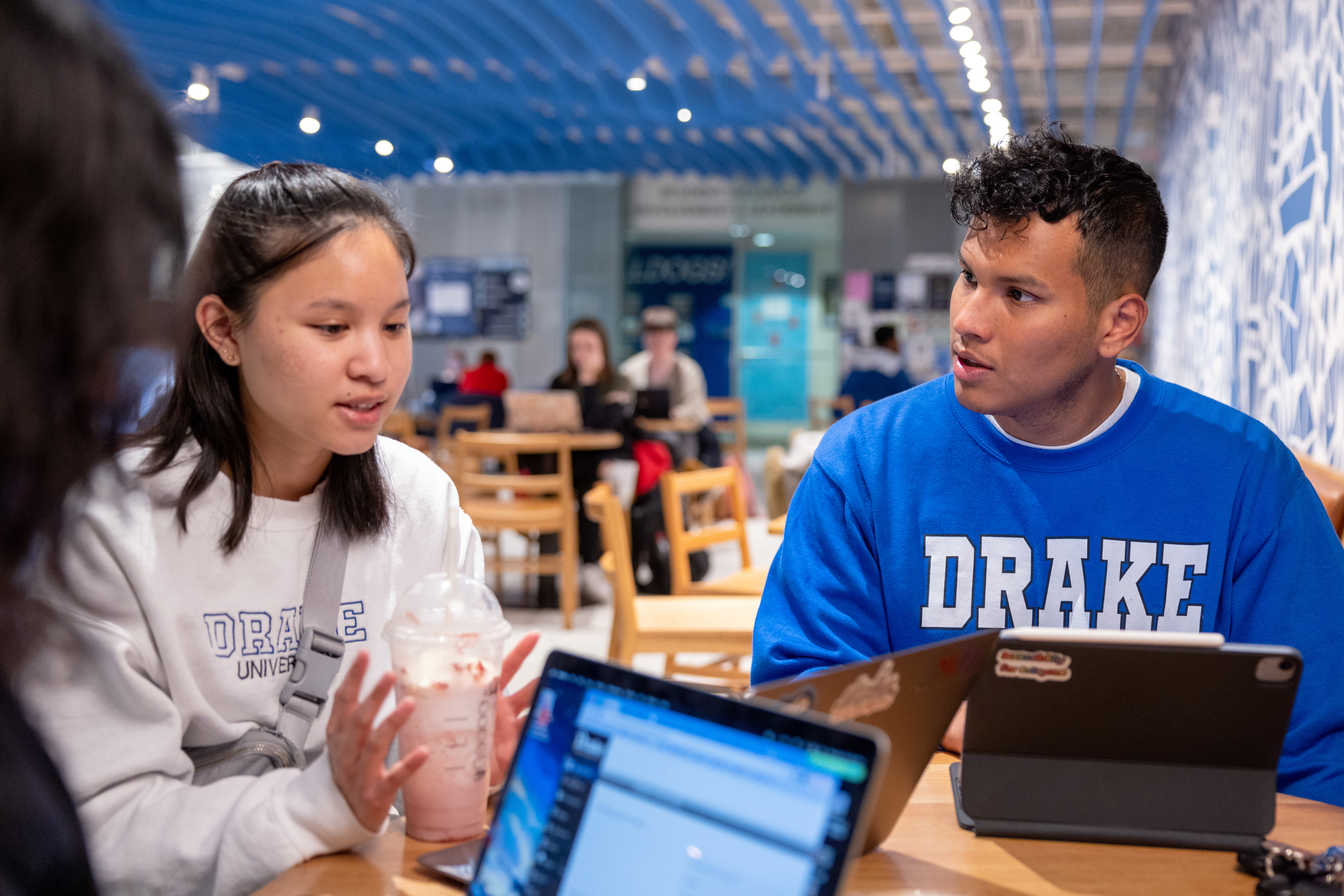 Several student sit around a table in a dining establishment on campus with laptops and beverages on the table