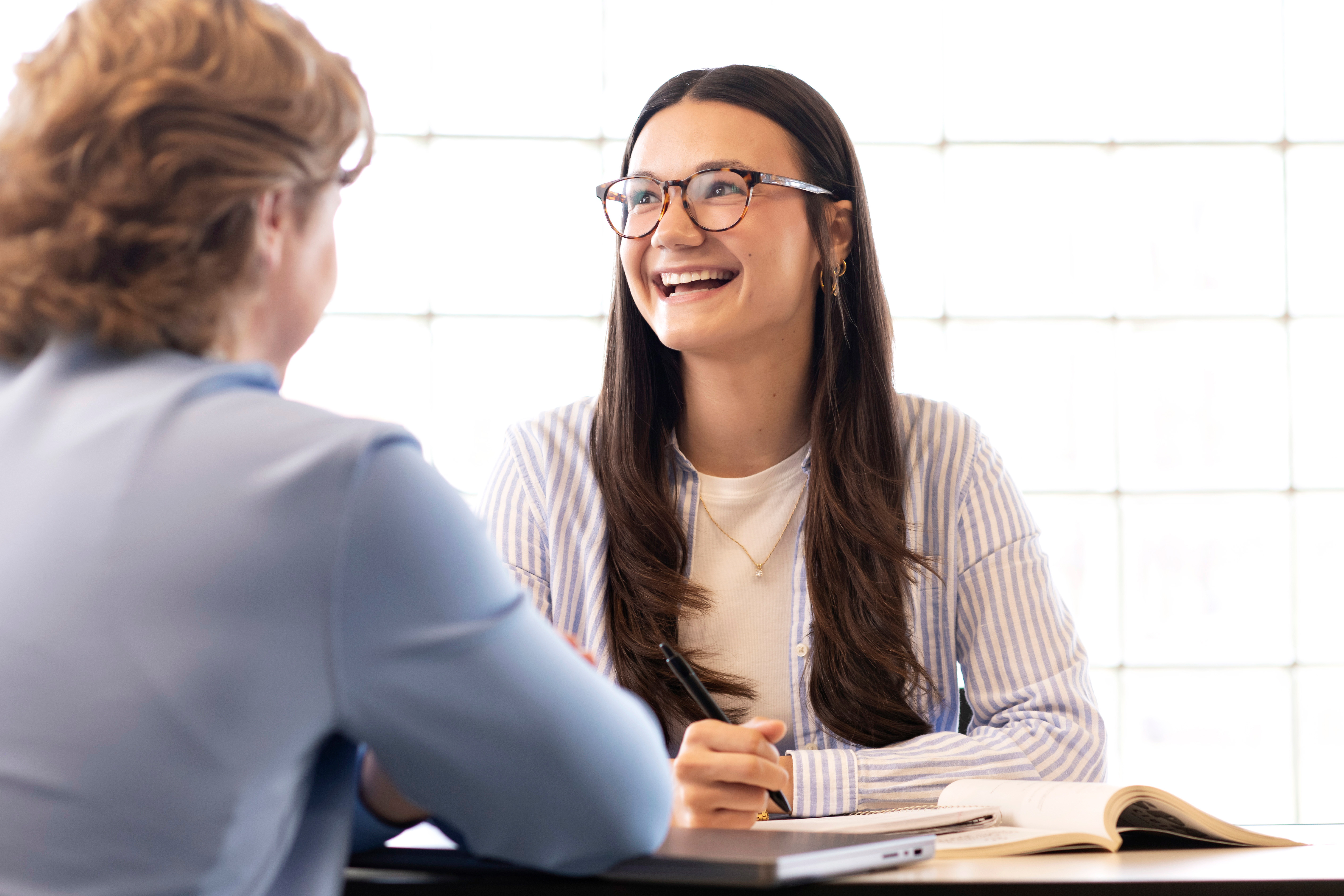A student smiles looking off to the side with another student in foreground facing away from camera