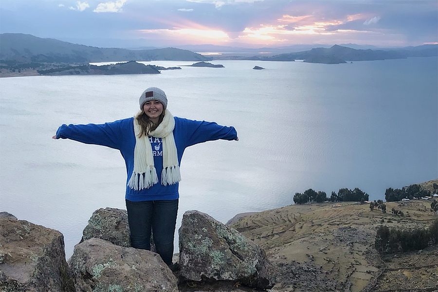 A student stands with arms outstretched with mountainous landscape in the background