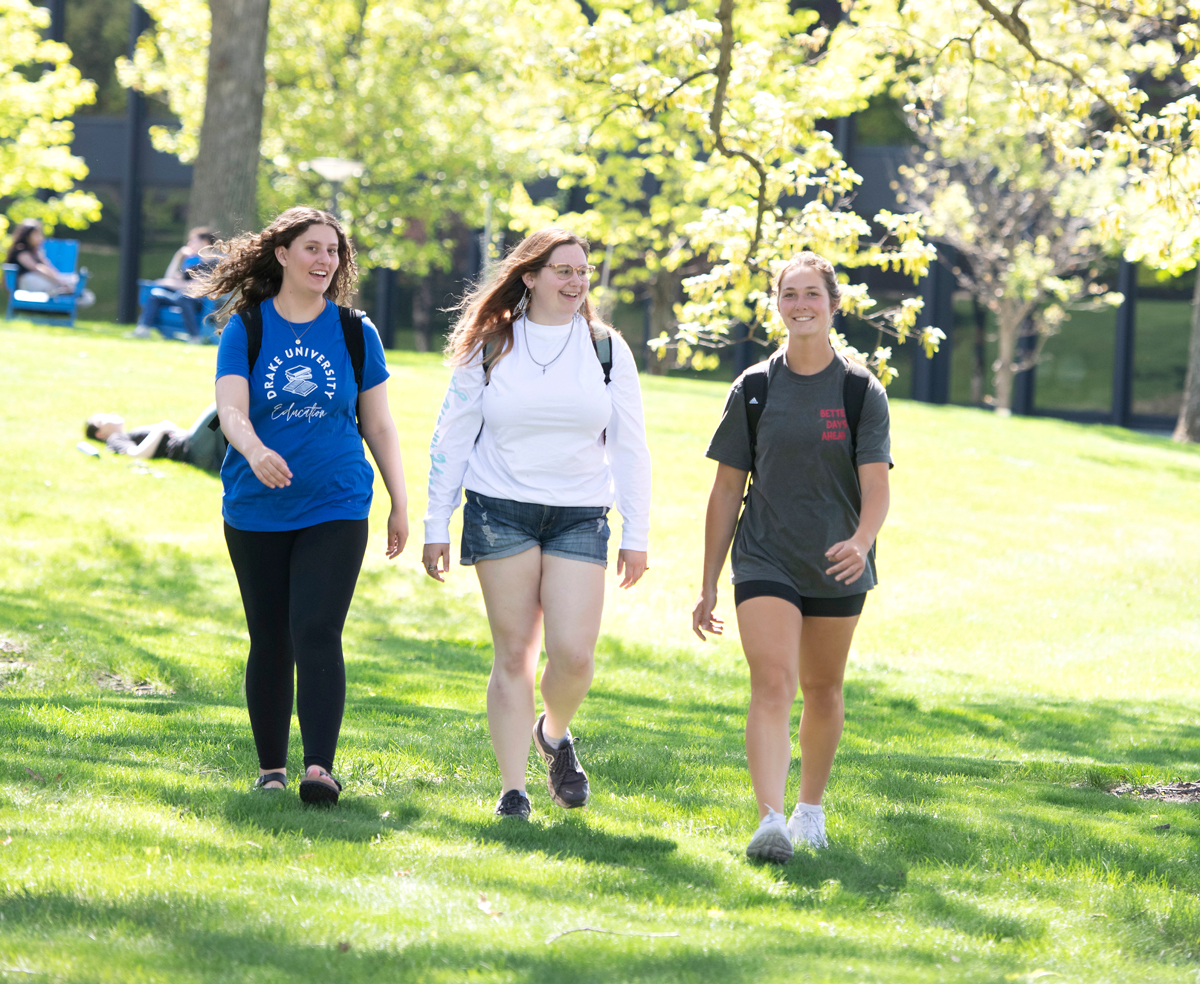 Three students walking across the grass on campus