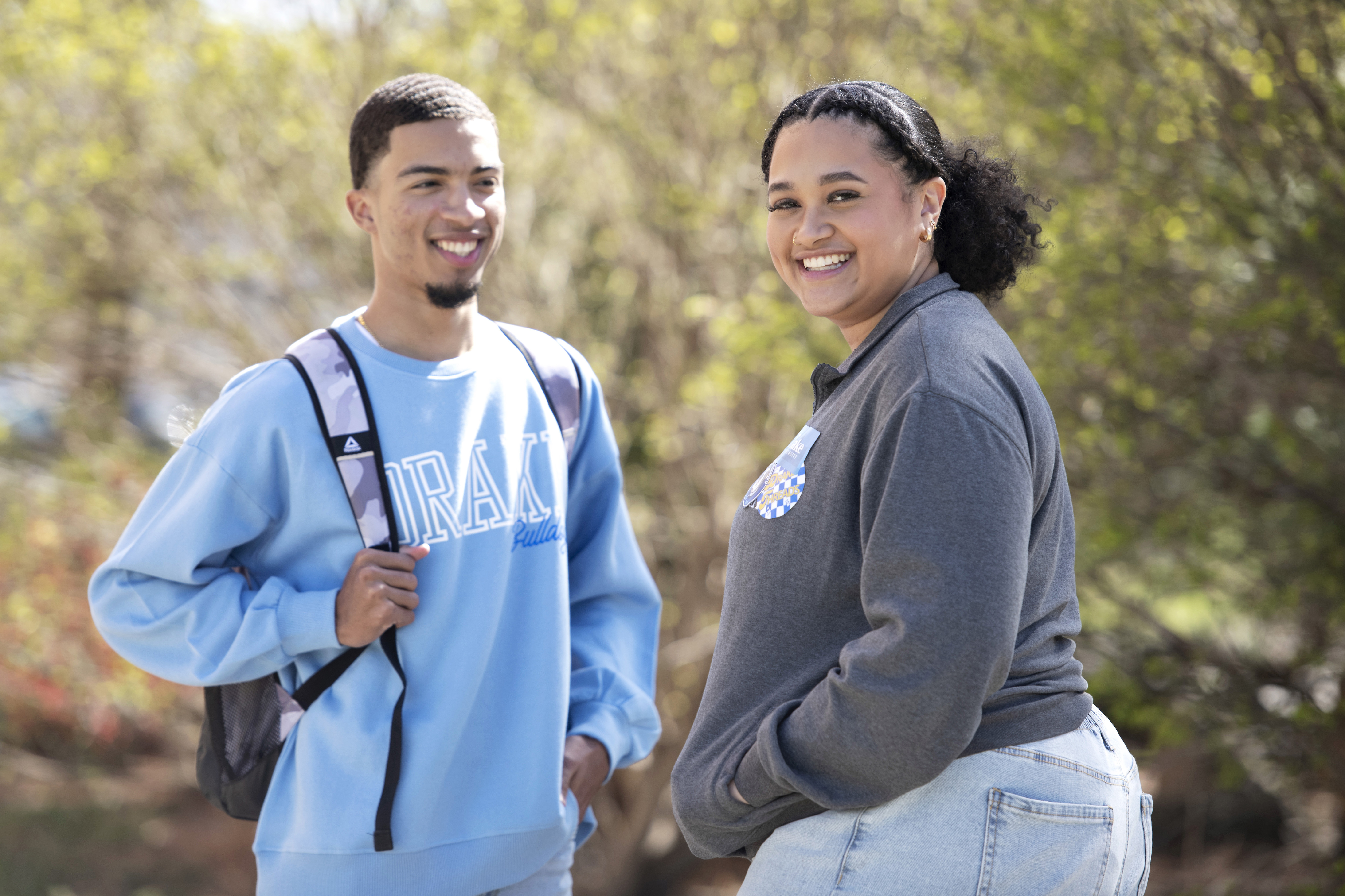 Two Drake students in school sweatshirts smile while having a discussion outdoors