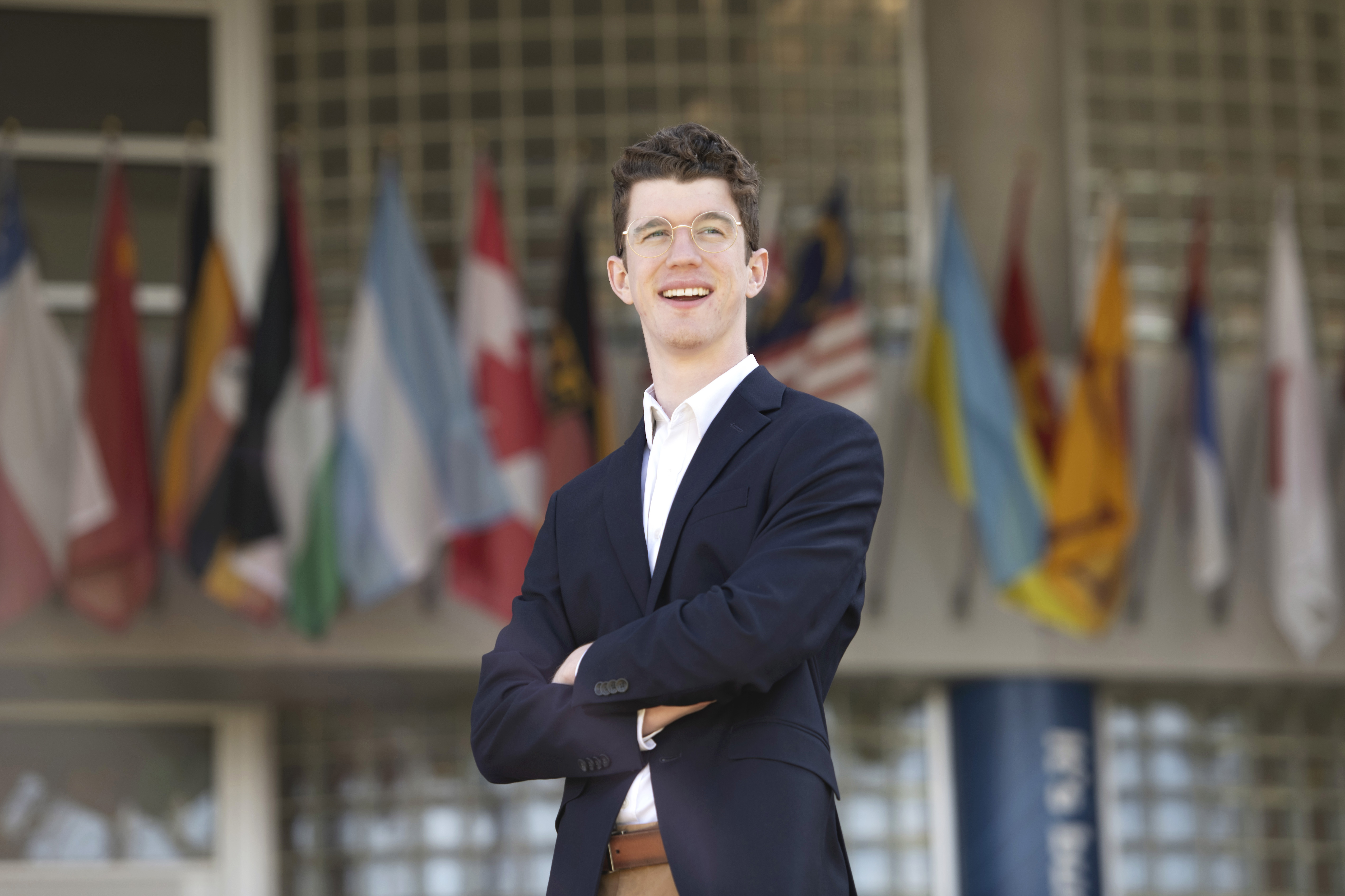 A student in a blazer crosses their arms while standing in front of Drake's Zimpleman College of Business