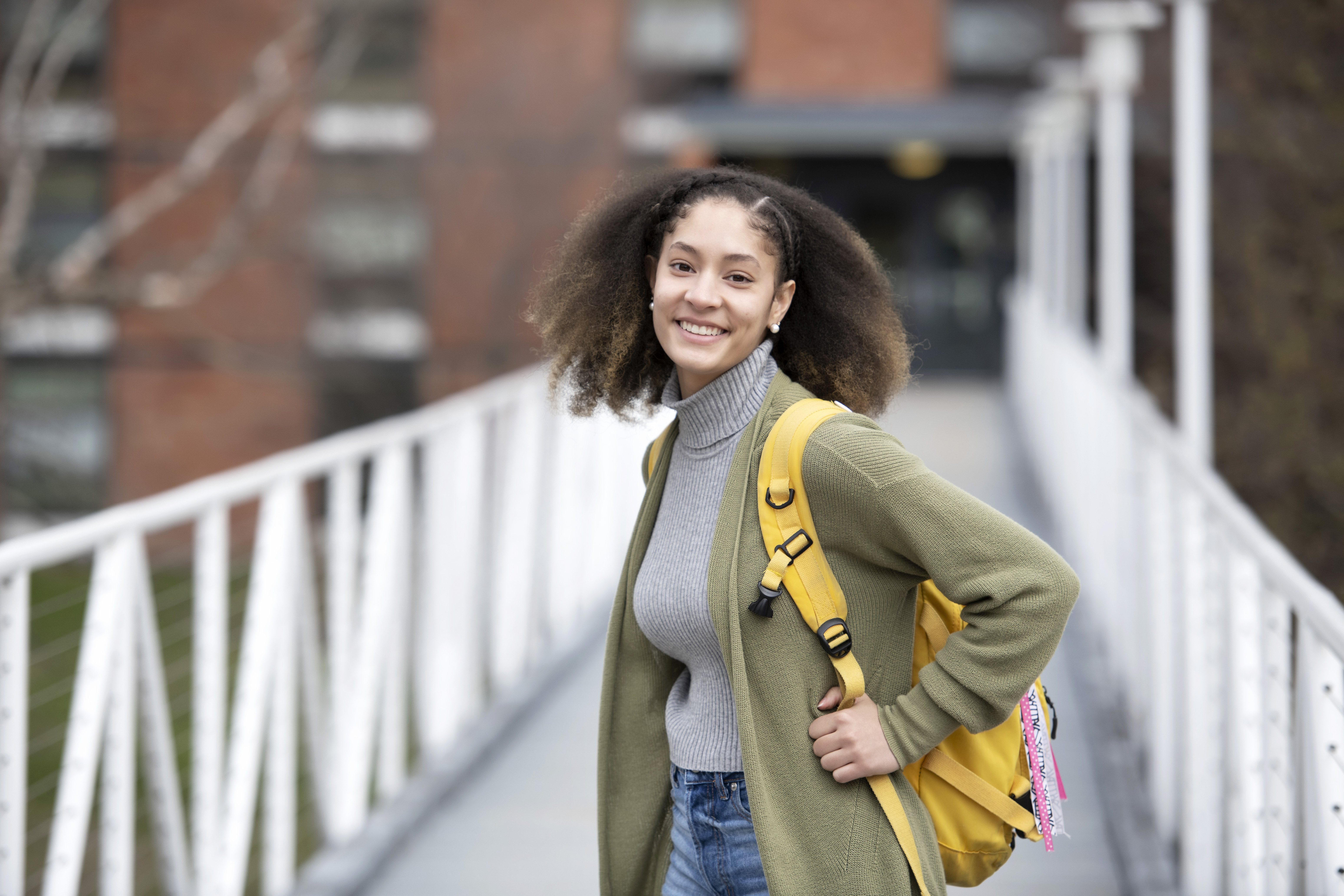A Drake first-year student with a backpack looks backward while crossing a bridge on campus