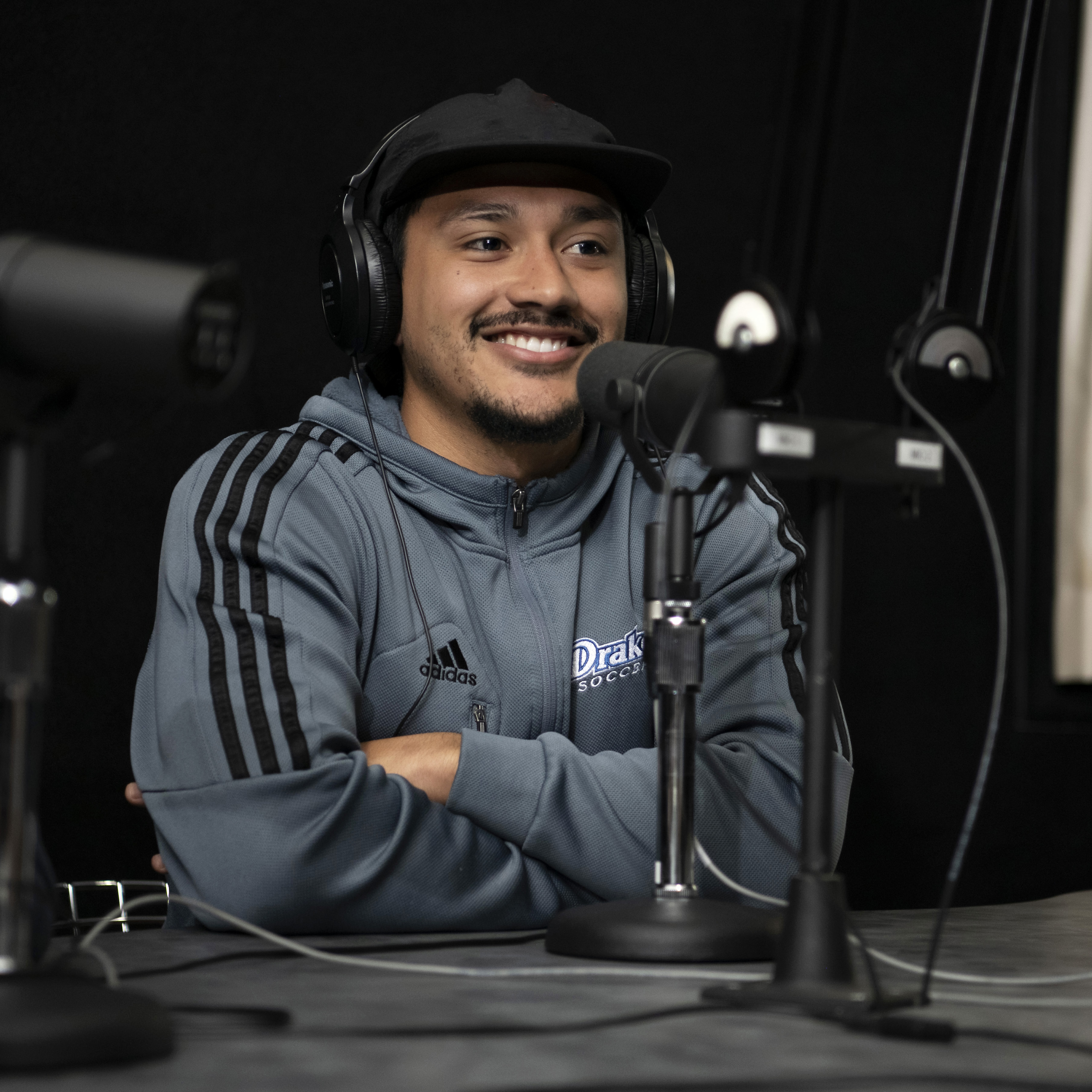 A student podcaster wearing a track jacket and cap waits for their turn to speak in one of Drake's media labs