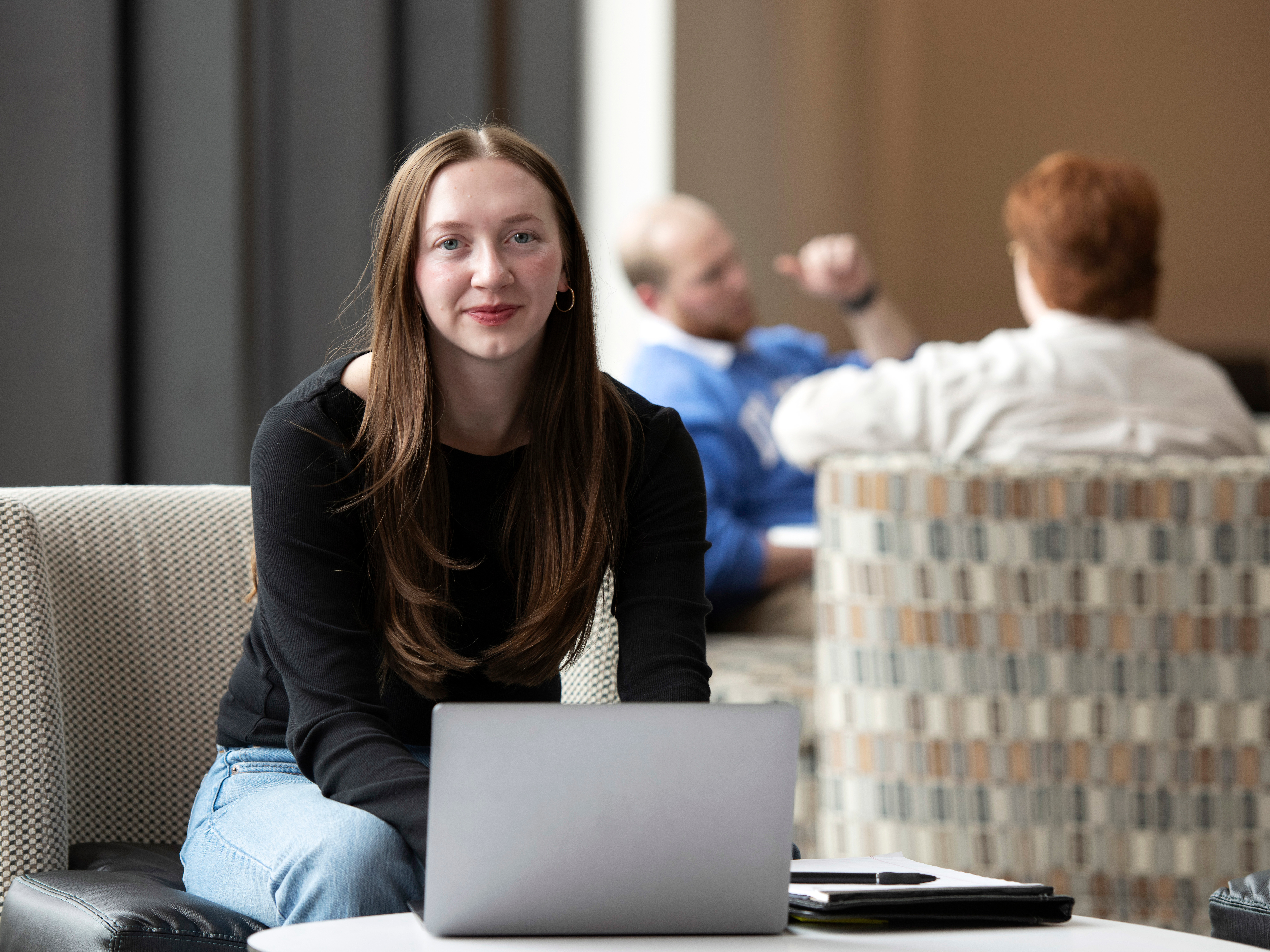 A Drake student completes an assignment on a laptop, notebook open on a table in a common area