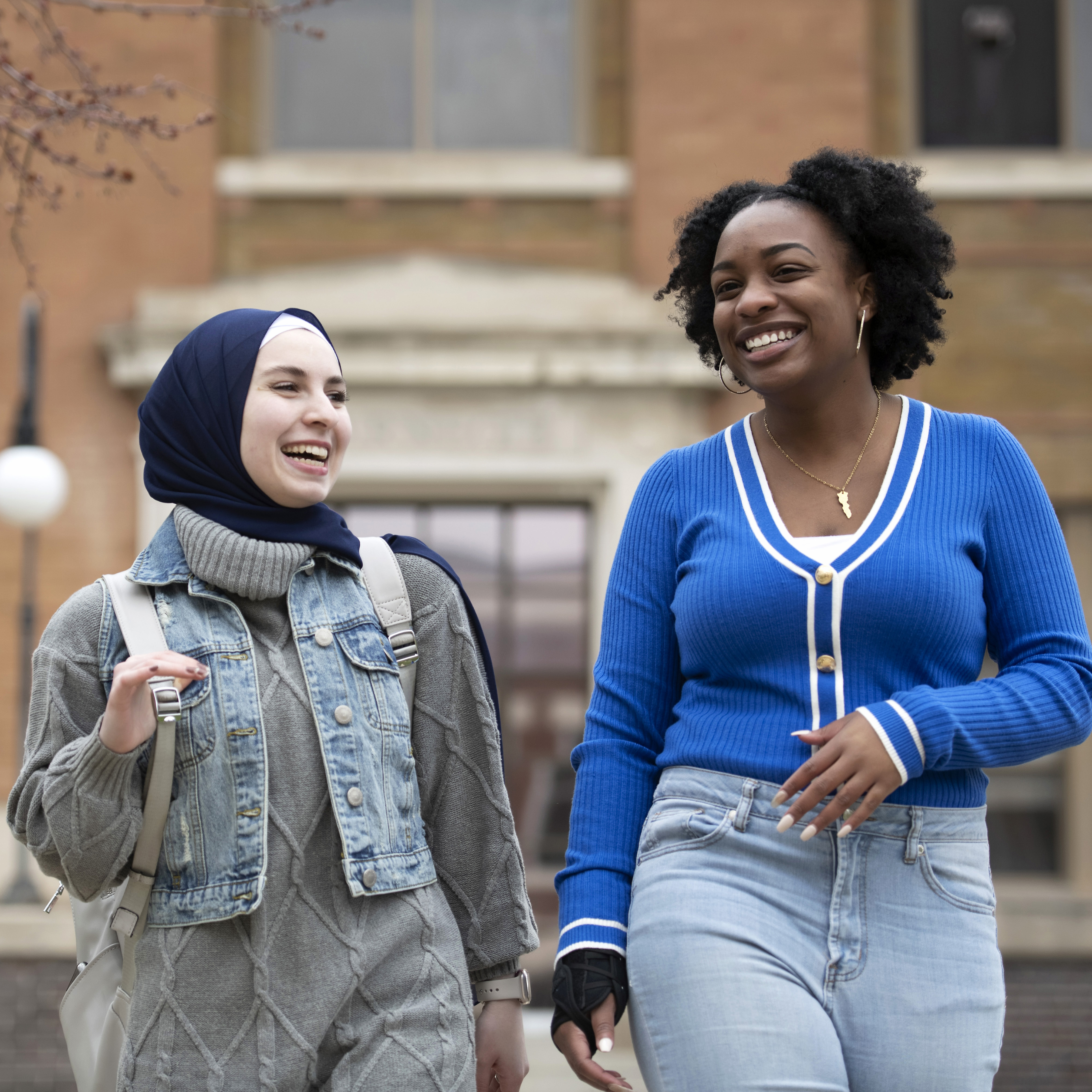 Two Drake international students, one with a backpack, walk leisurely near a brick building on campus