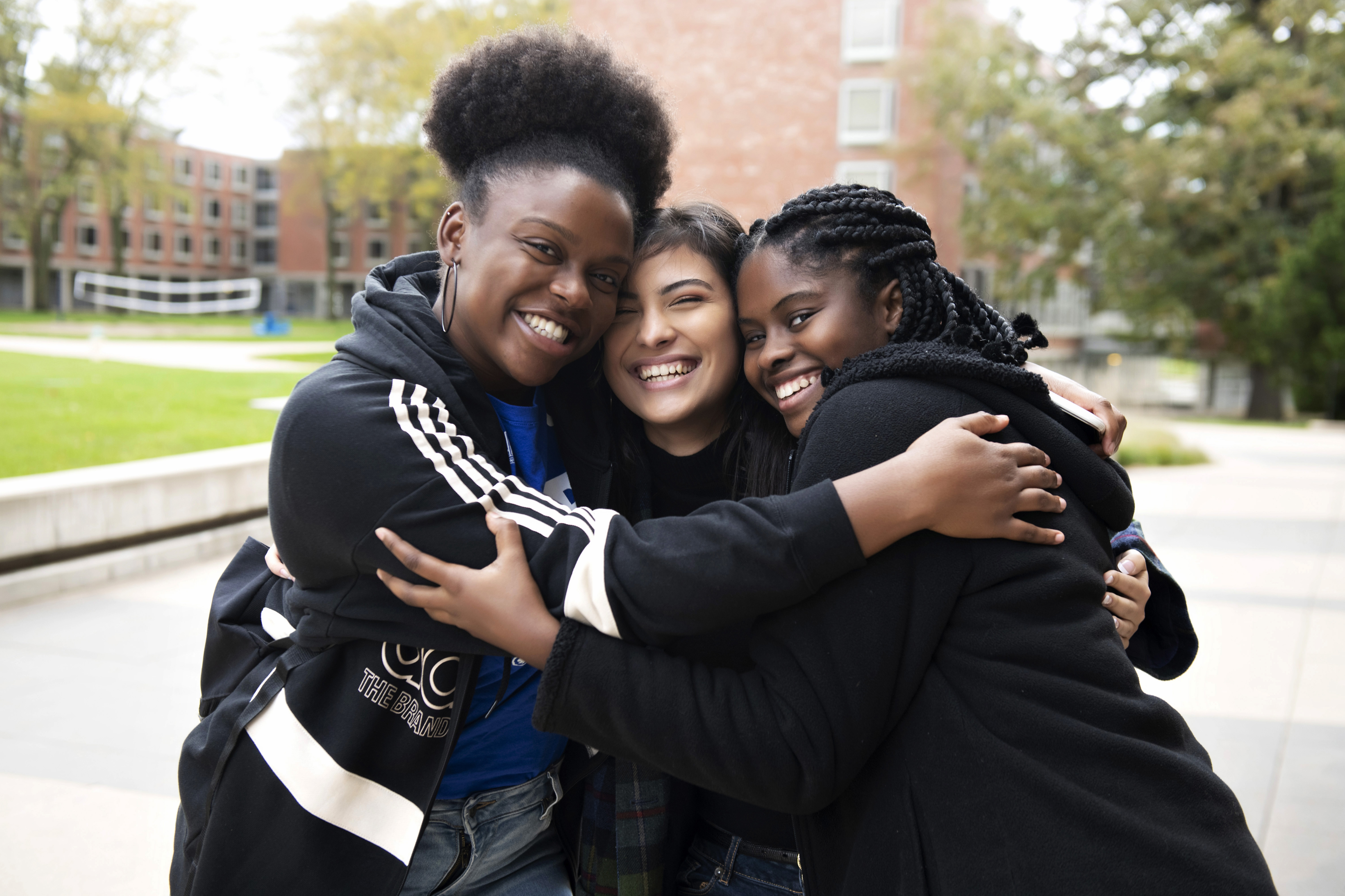 Three international students hug on a path near one of Drake's residential communities