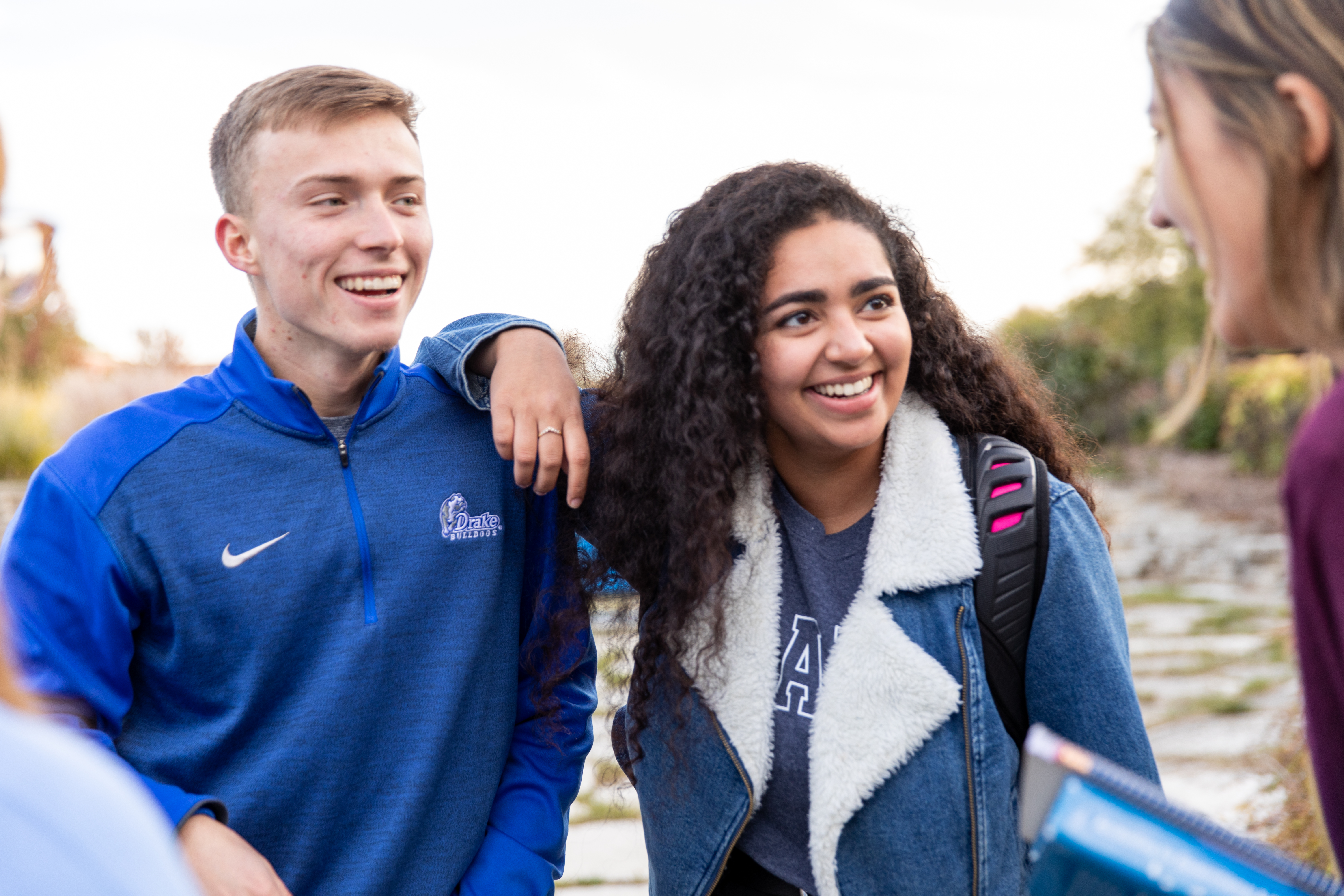 Outdoors, two Drake international students lean on each other while listening to a fellow student