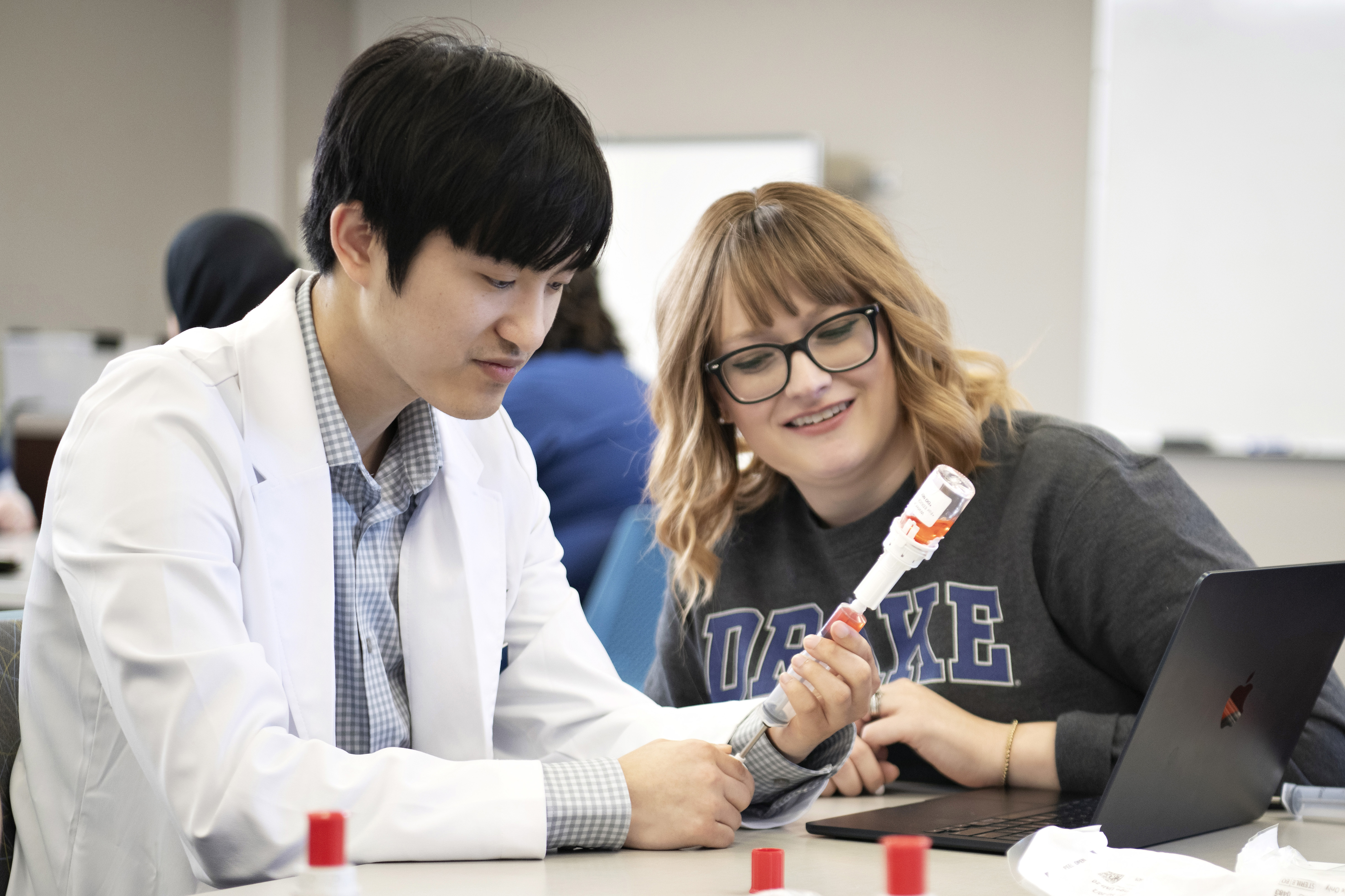 Two Drake students practice drawing medication from a vial in a pharmacy class