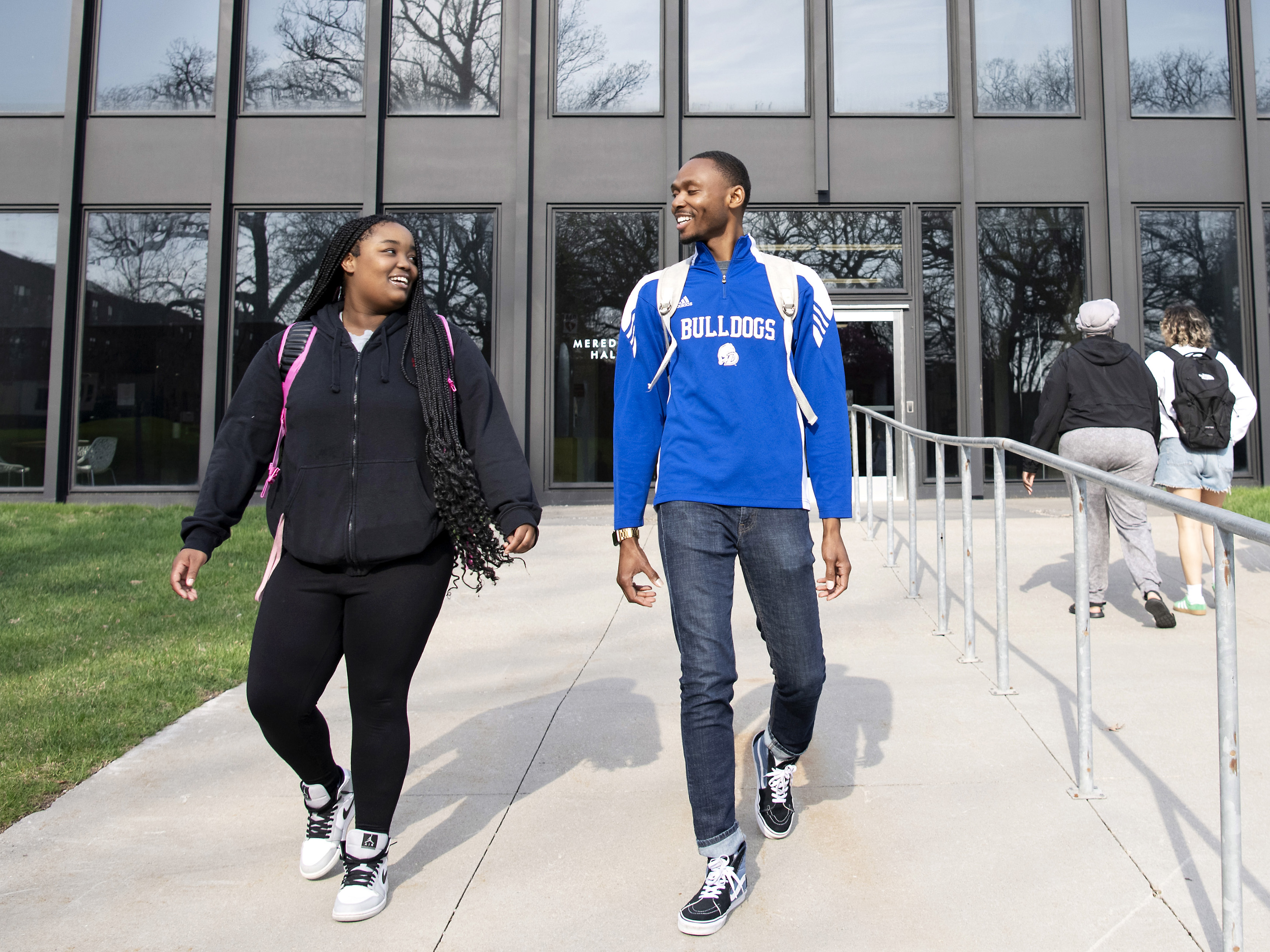 Wearing backpacks, two Drake transfer students glance at each other as they depart a classroom building