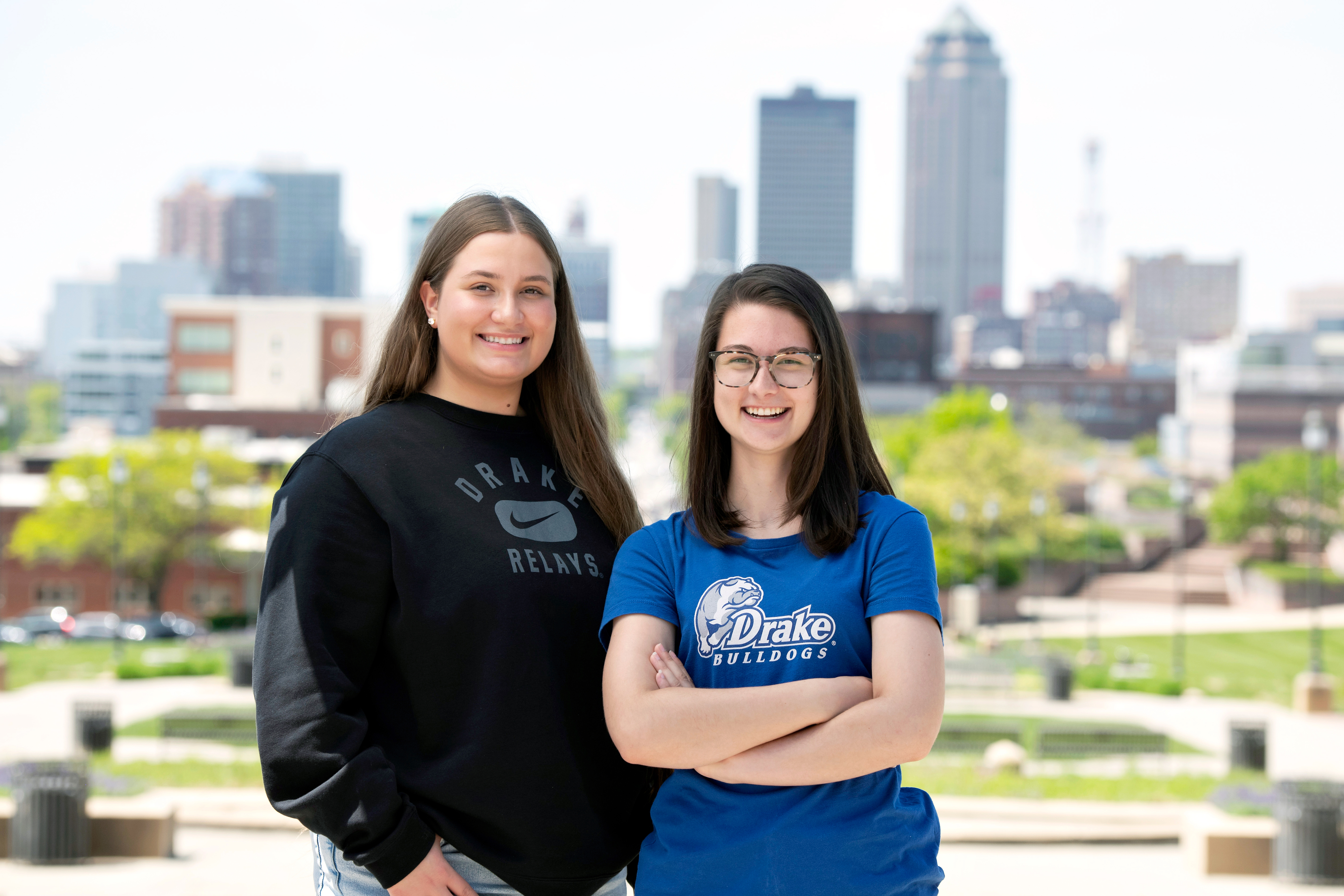 Two Drake transfer students in school garb stand and smile in front of the Des Moines skyline