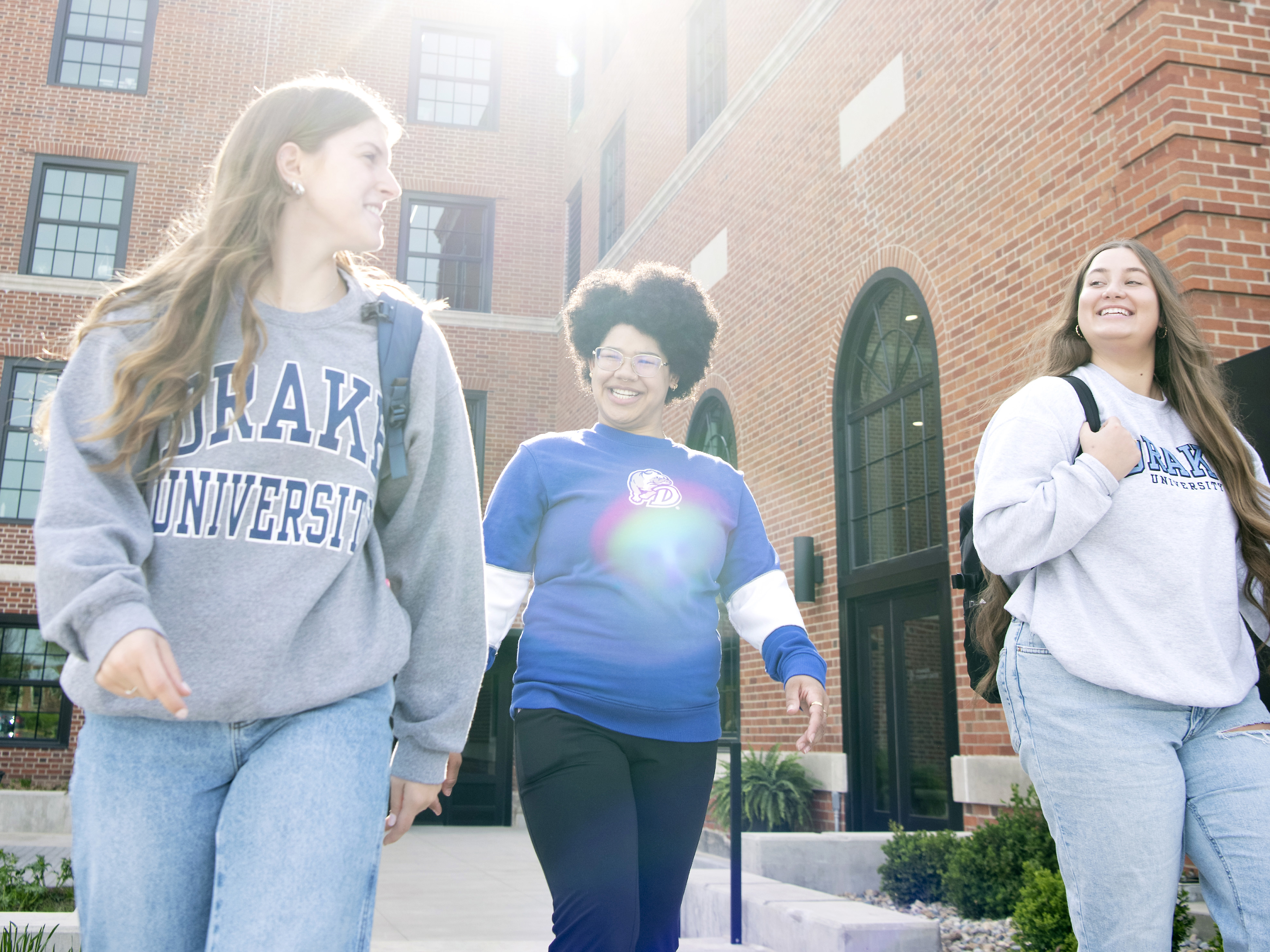 Three Drake transfer students, two with backpacks, walk and socialize between classes on a sunny day