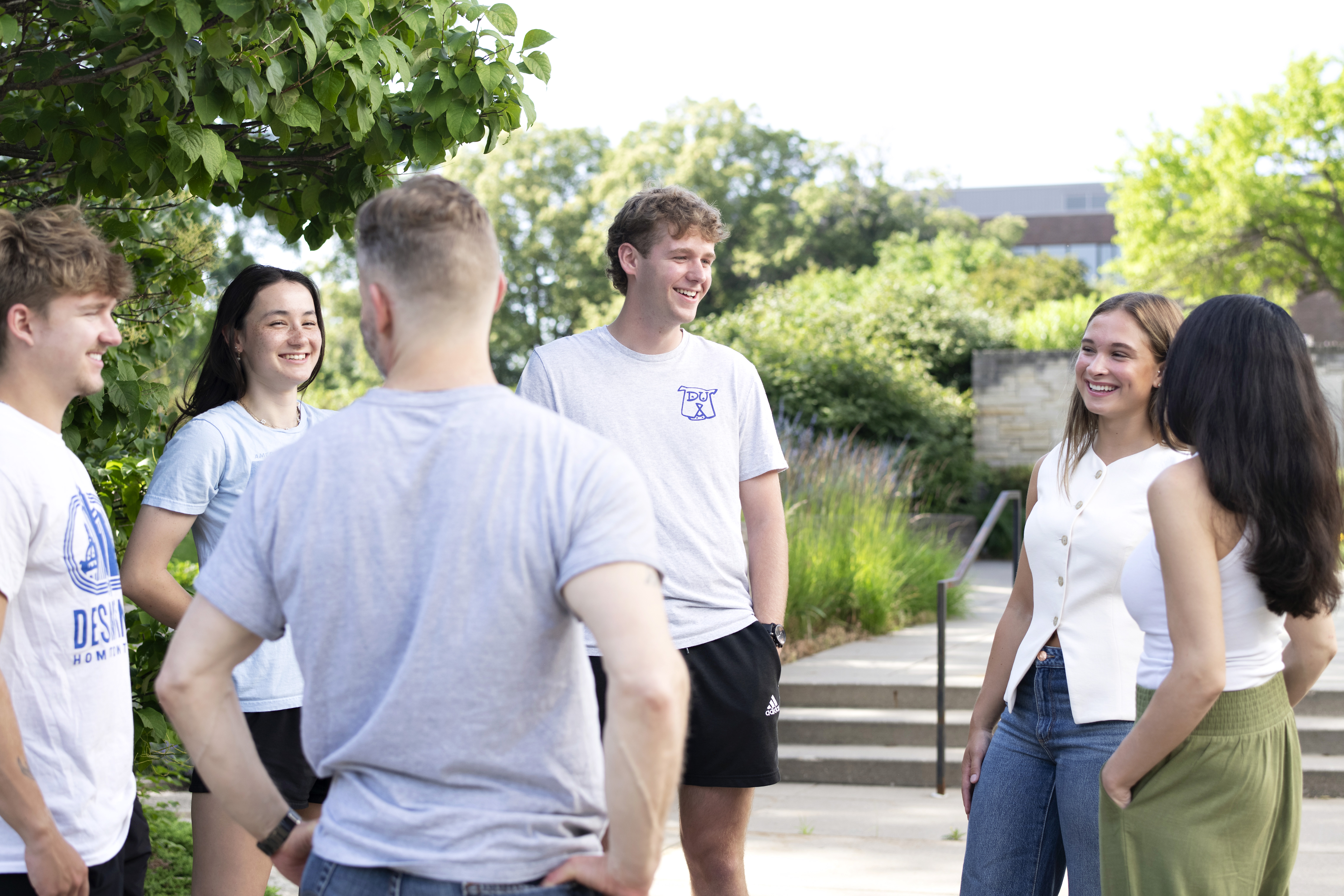 A group of prospective transfer students discusses the benefits of attending Drake during a group tour through an area of campus with trees and bushes