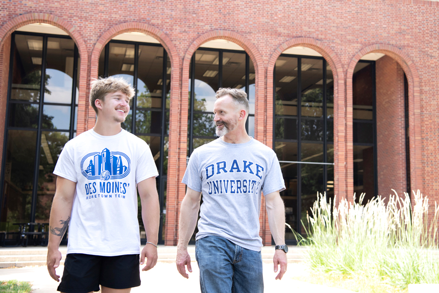 Two individuals look at each other, smiling, while walking outside on campus