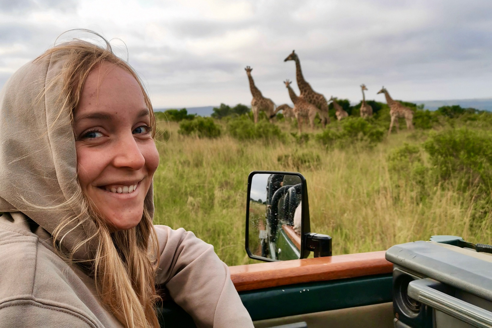 A student smiles at the camera with giraffes in the background on a safari study abroad trip