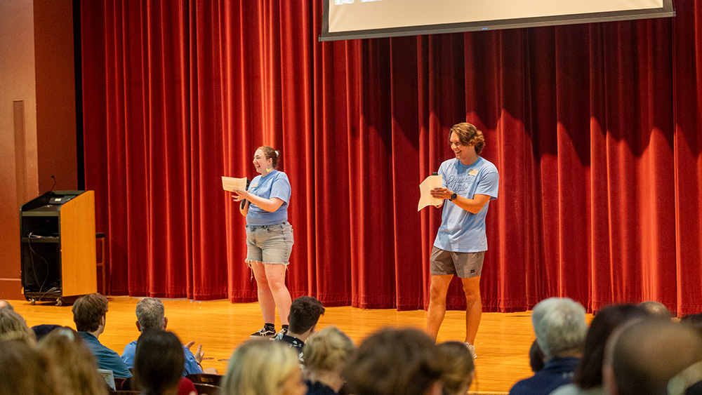 Two student orientation leaders laughing on stage in Sheslow while leading a Summer Orientation session.