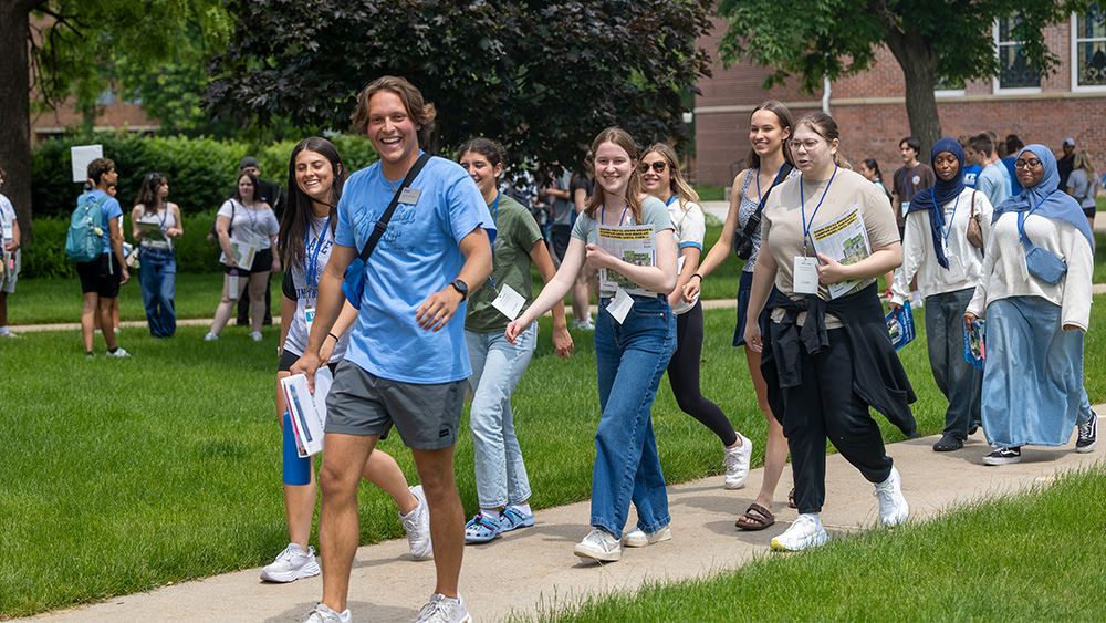 A student orientation leader walking with a group of students across campus.