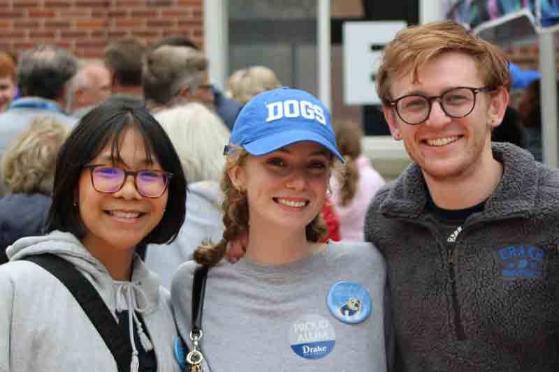 Three Drake alumni wearing shirts in varying shades of gray smile while standing arm and arm at an event.