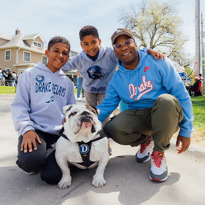 A Drake alum with their children squats down to pet Griff II, the school mascot, during the Drake Relays