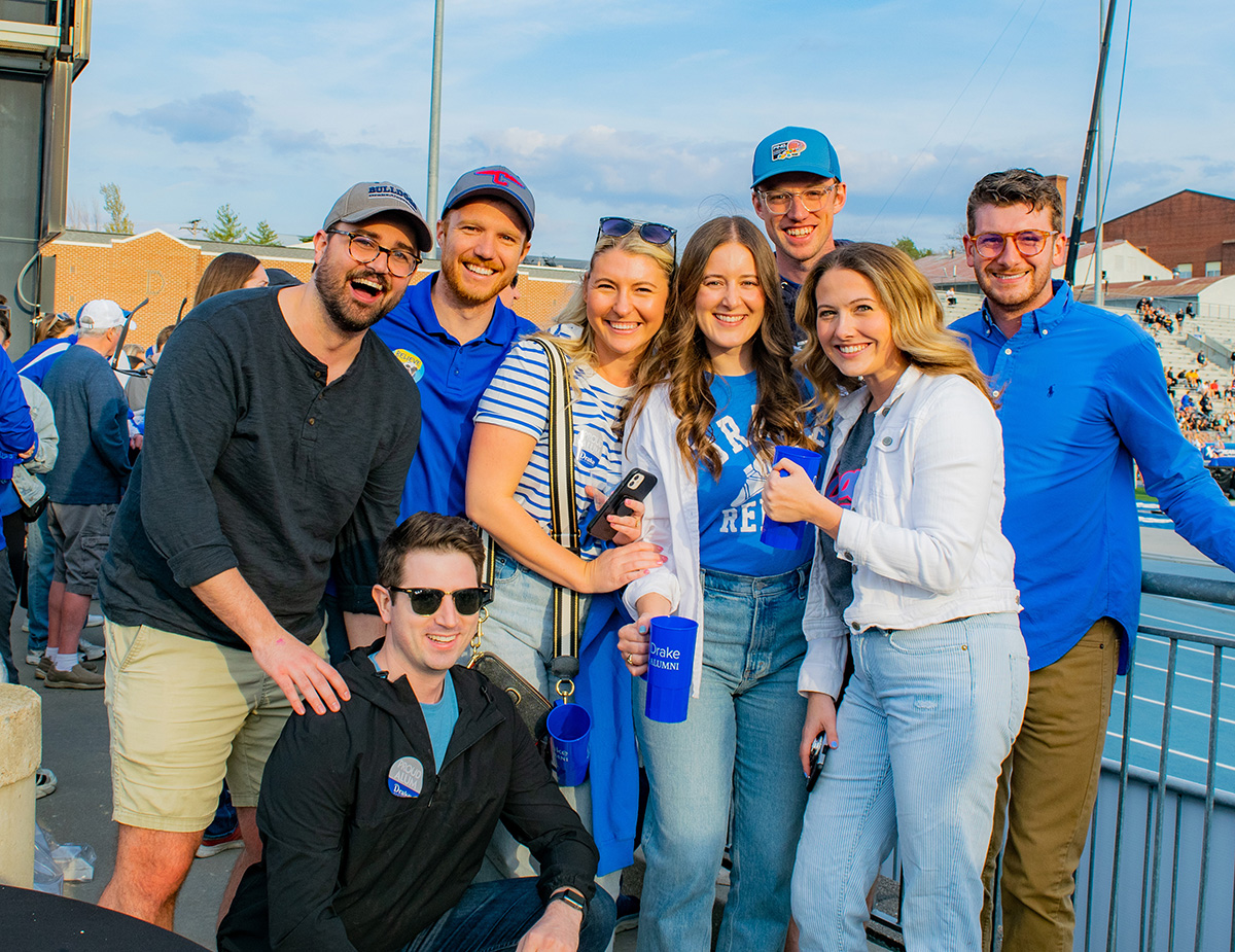 Drake alumni in varying shades of blue huddle near the track during the Drake Relays
