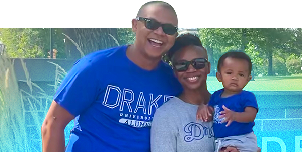 Family with man, woman, and baby standing on campus.
