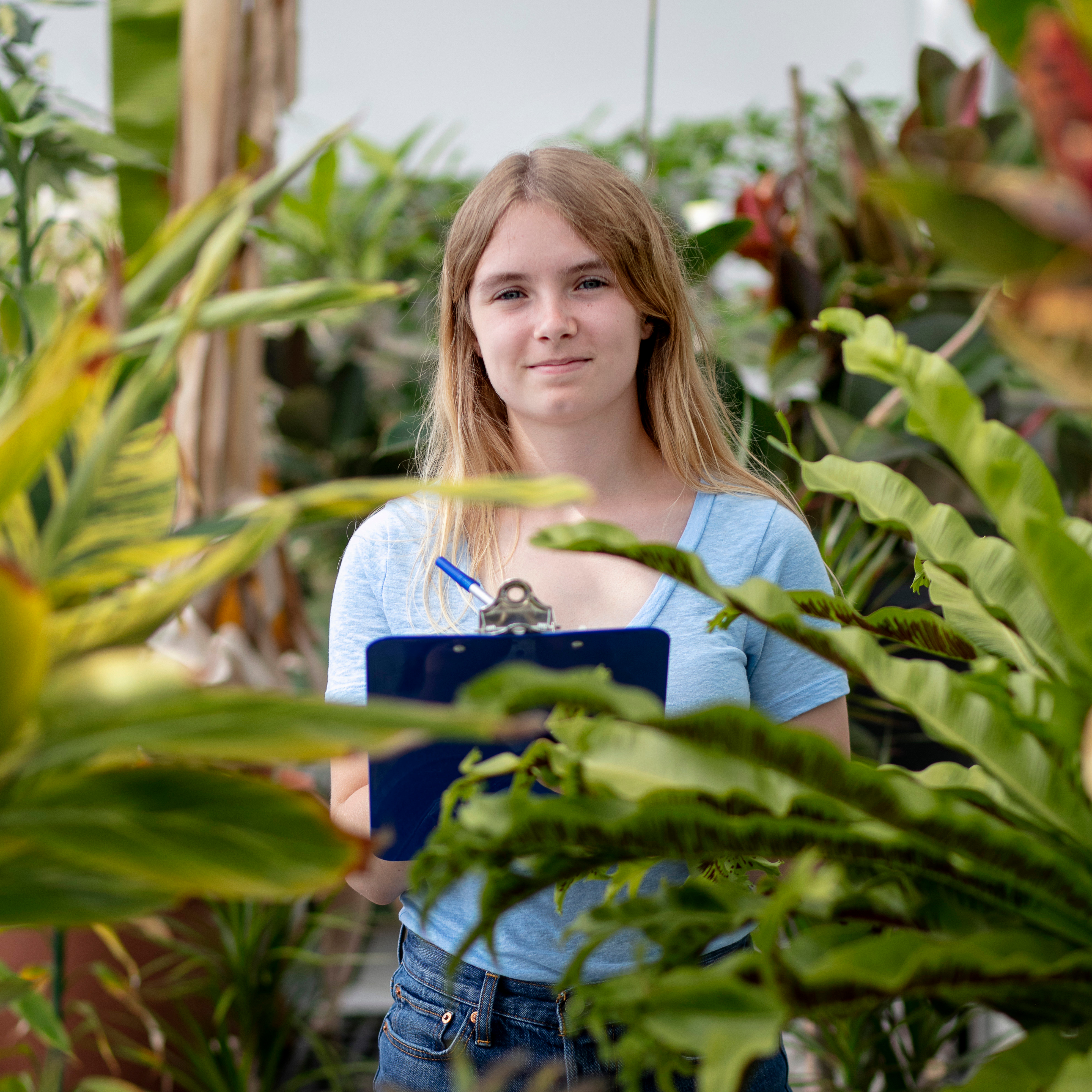 A Drake College of Arts and Sciences student takes notes on a clipboard in a leafy area
