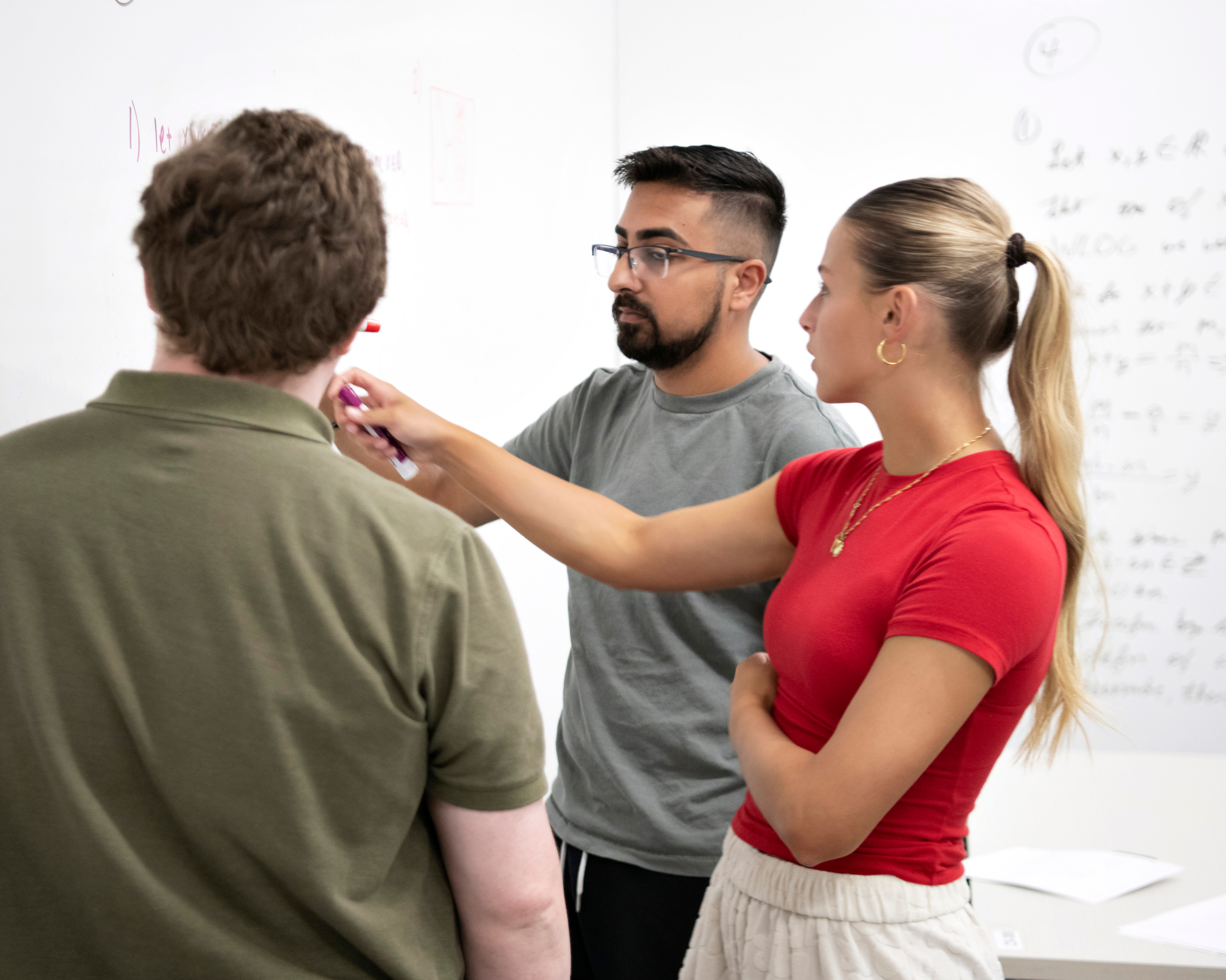 Three Drake students work on a math problem, standing in front of a whiteboard to devise a solution