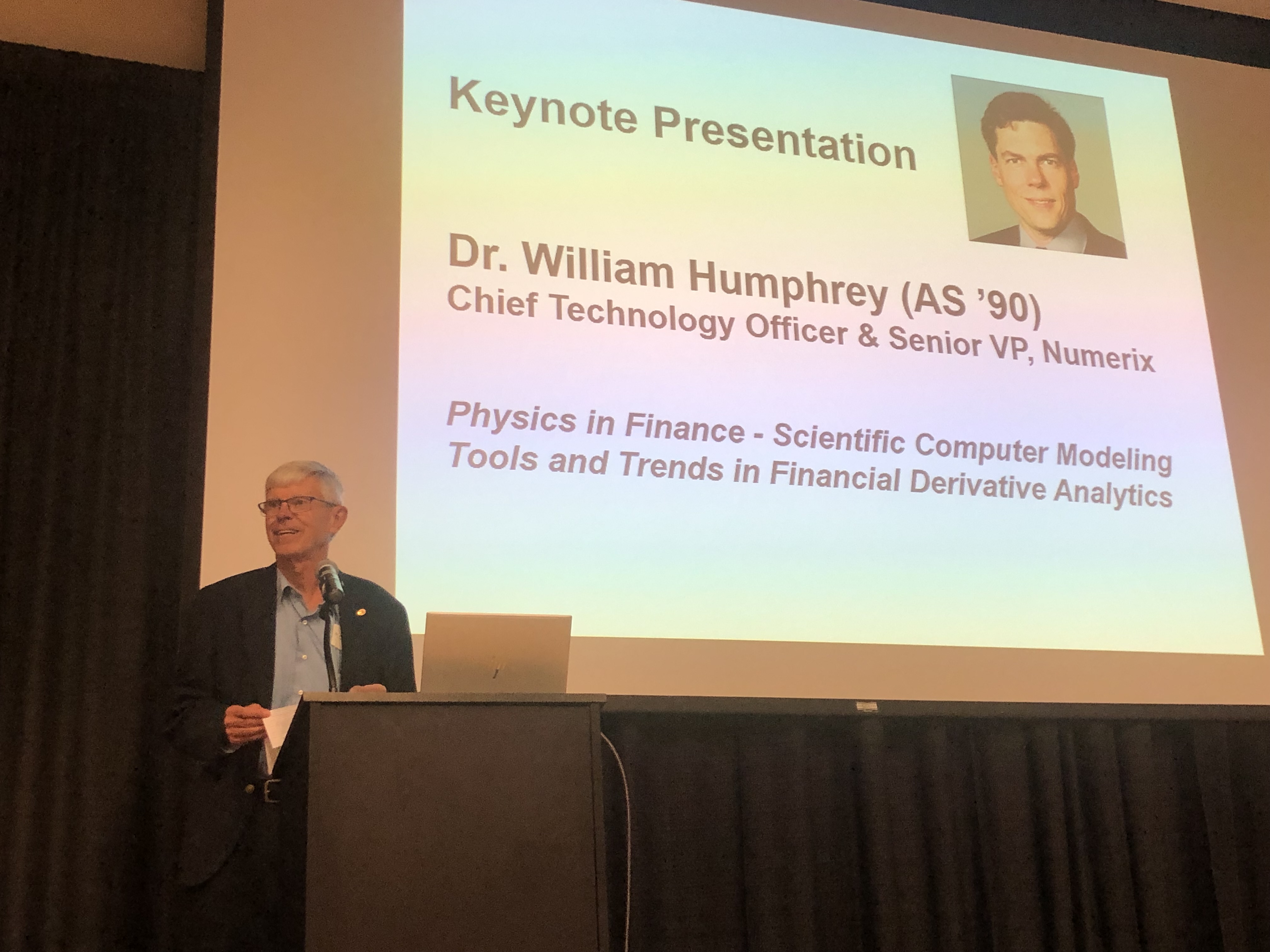 During the Life After Drake lecture series, a 1990 alum, standing behind a podium and near slides projected onto a screen, discusses their career progression to a group of Drake students