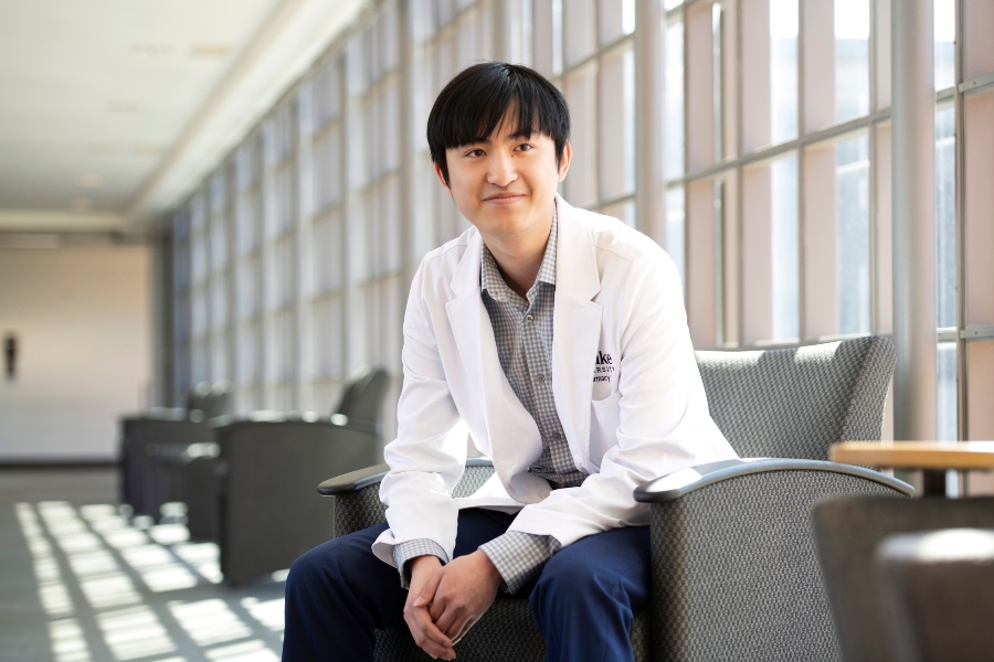 A Drake student in a lab coat leans forward while sitting in a chair in the College of Pharmacy and Health Sciences
