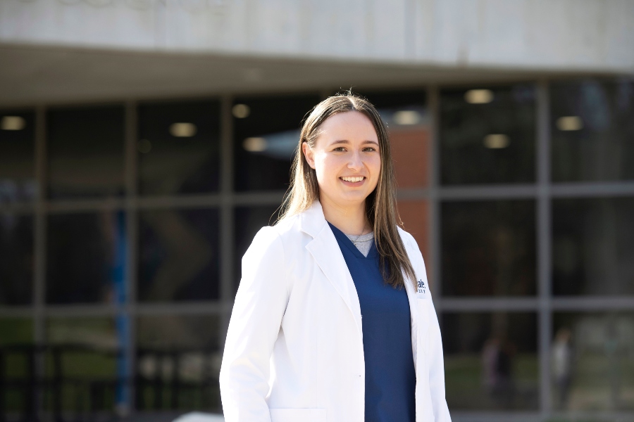 A Drake student enrolled in one of the College of Pharmacy and Health Sciences' residency or fellowship programs stands outdoors in a lab coat