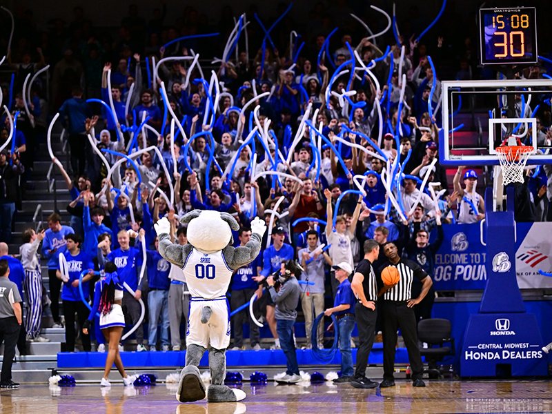 Drake students wave blue and white noodles as the Bulldog mascot encourages them to cheer during an NCAA Division I baseball game