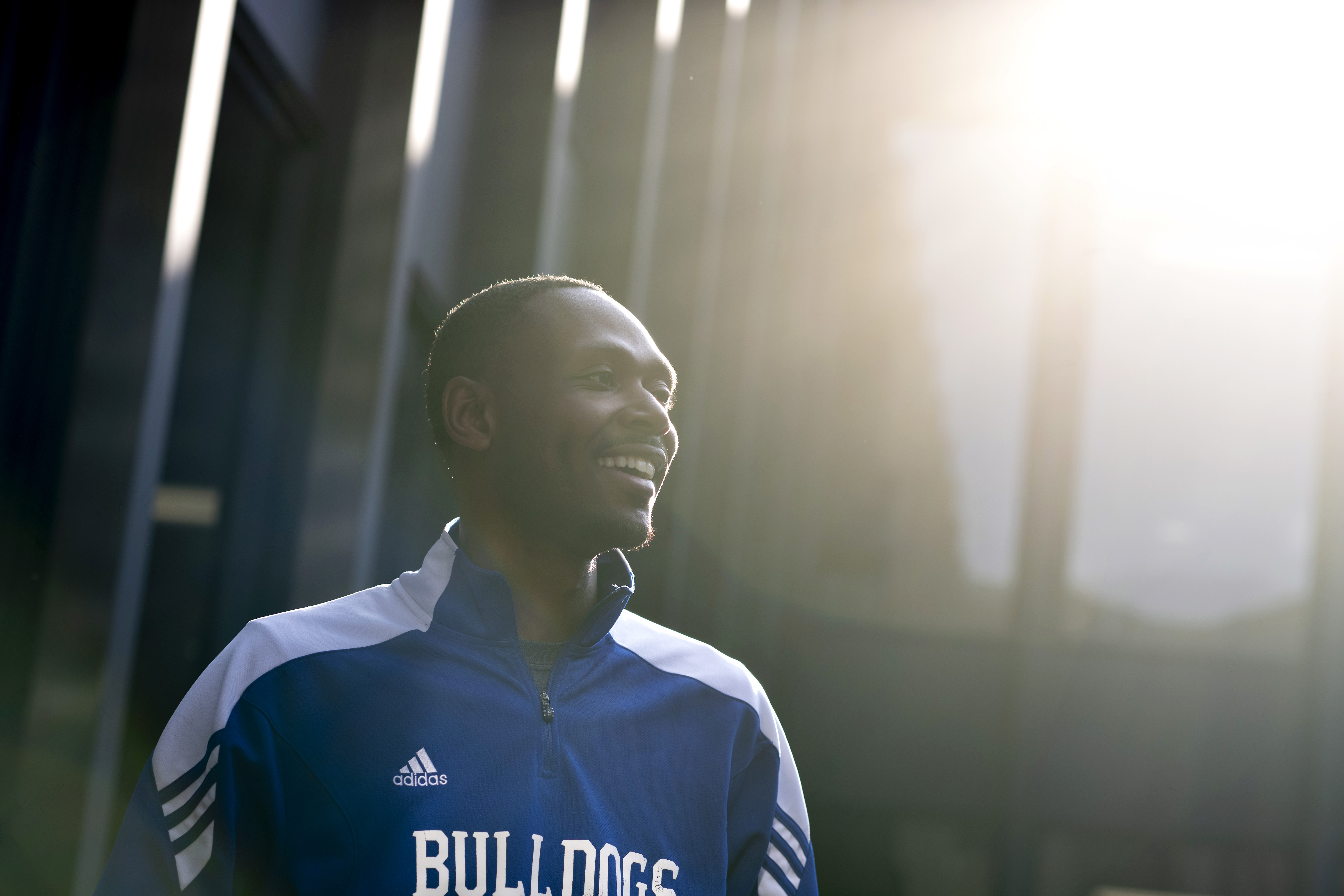A Drake student in a track jacket with the "Bulldogs" logo smiles while standing outdoors in the sunlight