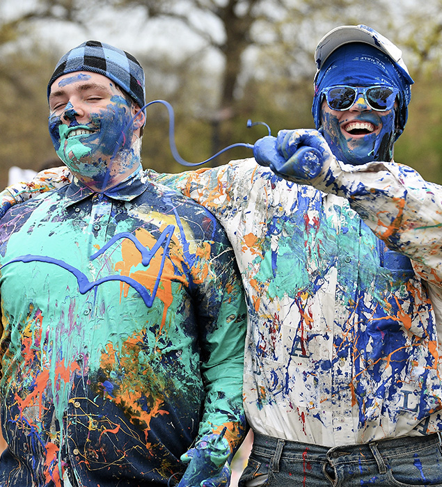 Street Painting - Two students smiling at the camera while one squirts paint at the other.